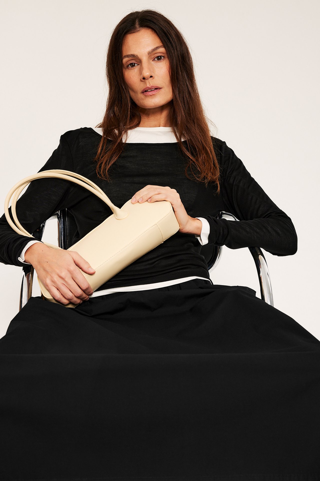 Kobieta w czarnej rozkloszowanej poplinowej spódnicy, czarno-białym topie, trzyma beżową torebkę.