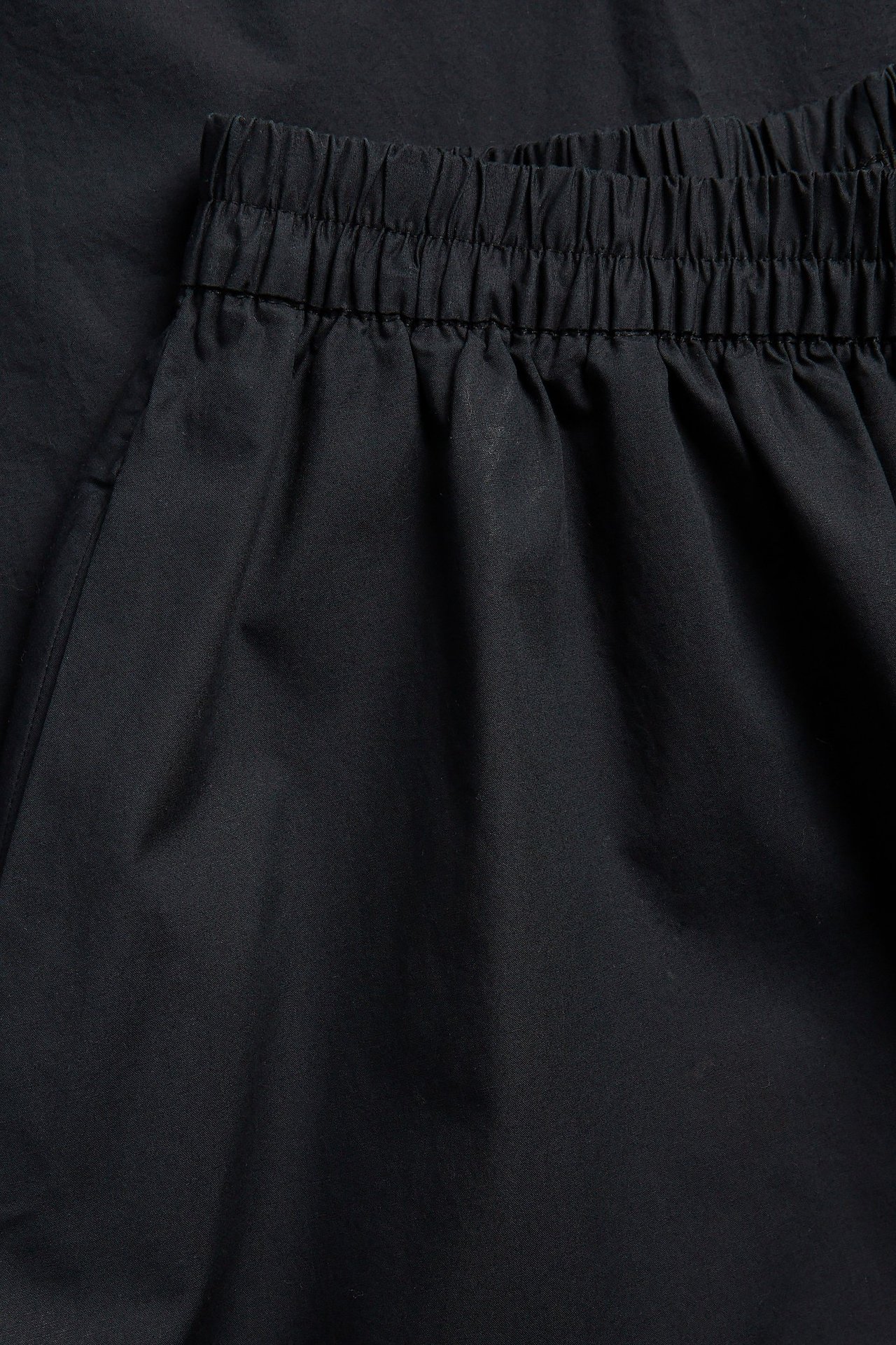 Zbliżenie czarnej bawełnianej spódnicy popelinowej z elastyczną talią i bocznymi kieszeniami.