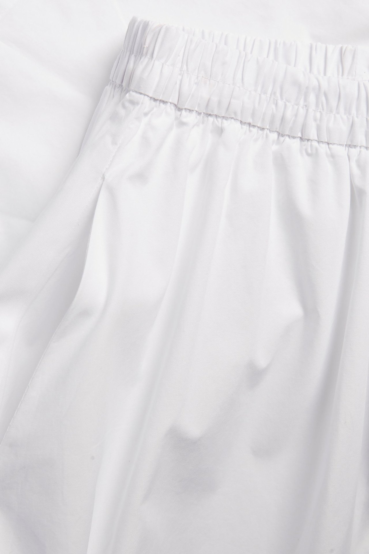 Zbliżenie białej, rozkloszowanej spódnicy z bawełnianej popeliny z elastyczną talią i bocznymi kieszeniami.