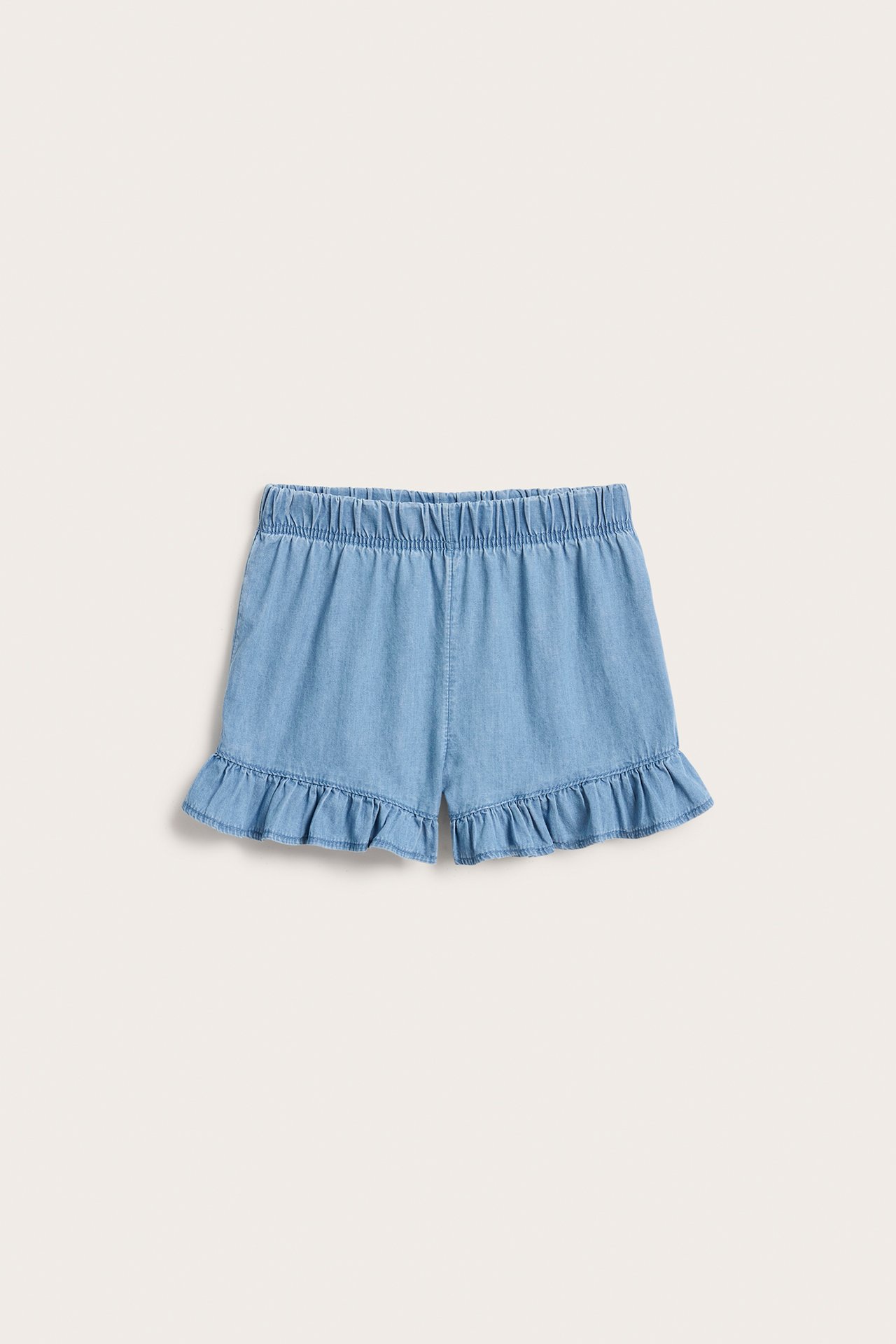 Frontvy av ljusa jeansshorts för barn med resår i midjan och volanger i bensluten.