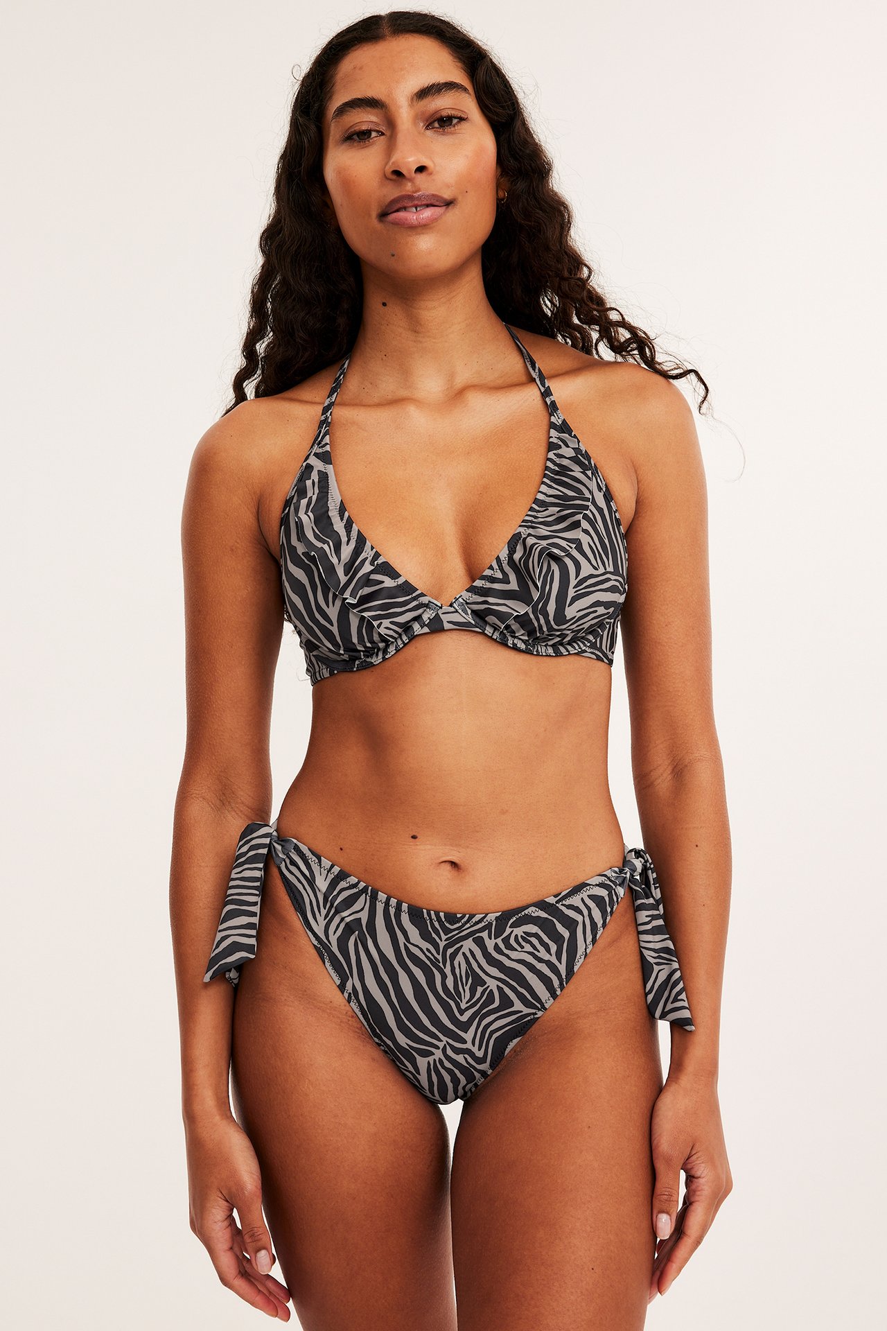 Frontbilde av en kvinne i svart og grå sebrastripet bøyle-bikinitopp og matchende knyte-bikinitruse.