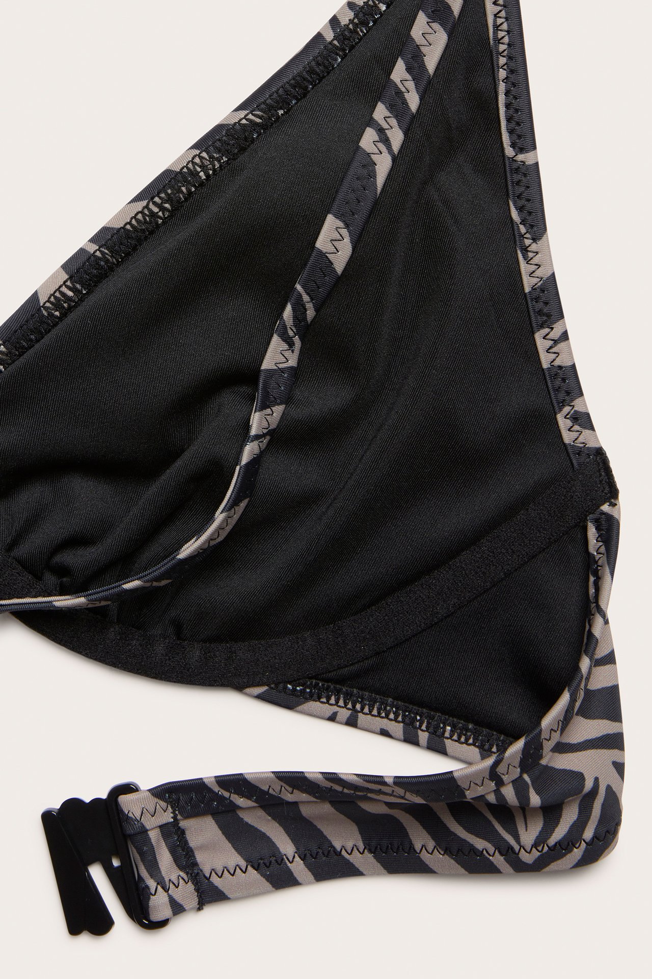 Nærbilde av en mørk beige og svart sebrastripet bøylebikinitopp med halterneck-knyting og ryggspenne.