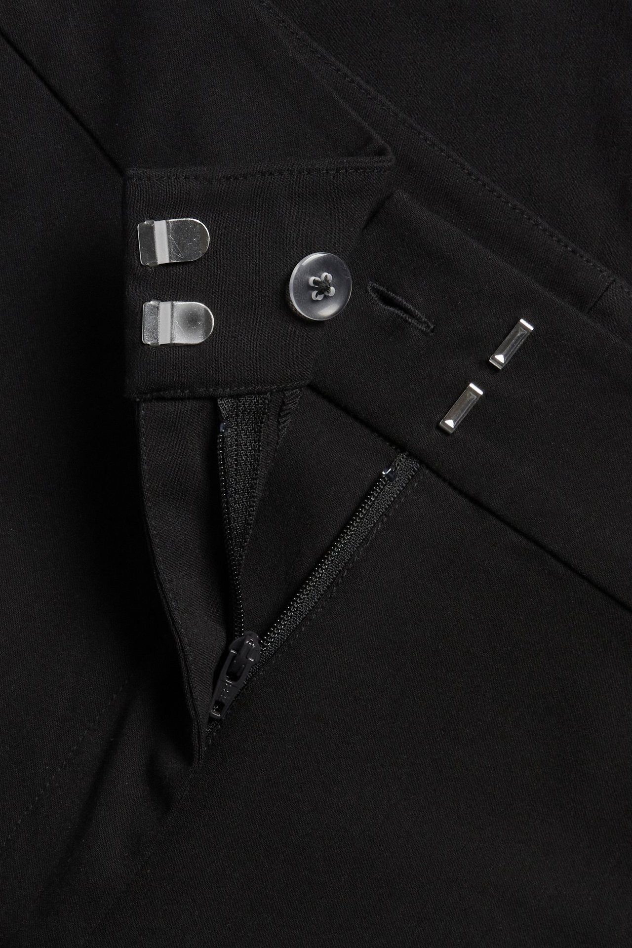 Zbliżenie czarnych szortów capri z zamkiem błyskawicznym, guzikiem i zapięciem na haftki.