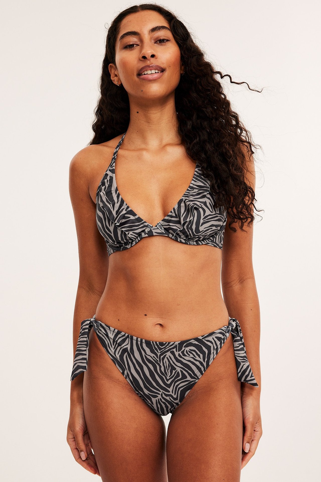 Widok z przodu: kobieta w ciemnobeżowych figach bikini Brazilian w zebrę z wiązaniami i pasującym topie halterneck.