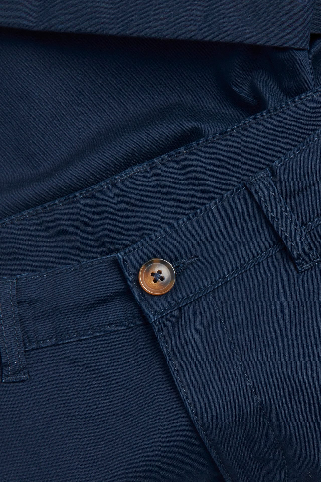 Nærbilde av mørkeblå ensfargede chinosshorts med brun knapp og glidelås.