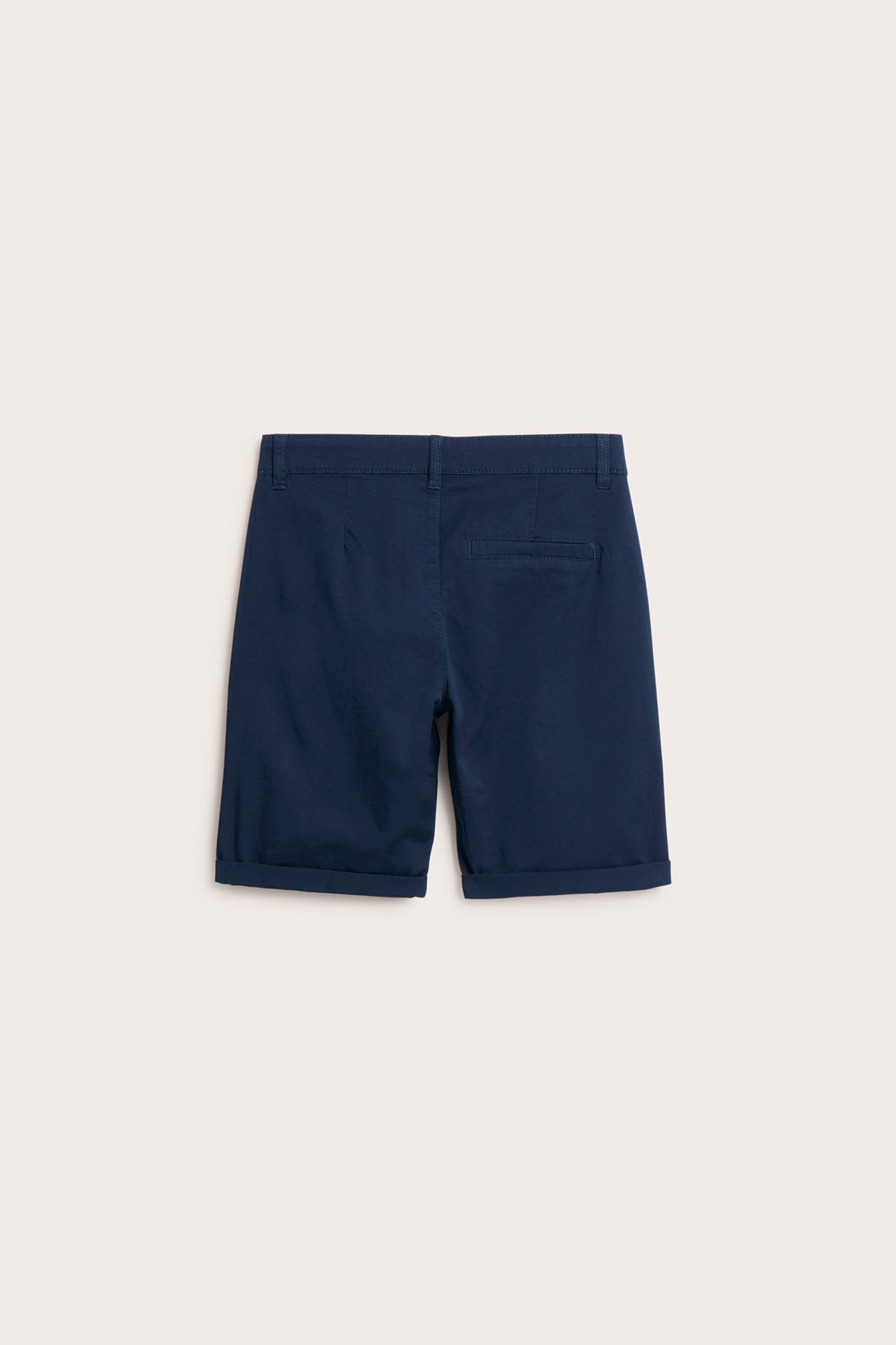 Bakfra, mørkeblå ensfargede chinosshorts i stretchbomull for barn med oppbrettede ben og en falsk baklomme.