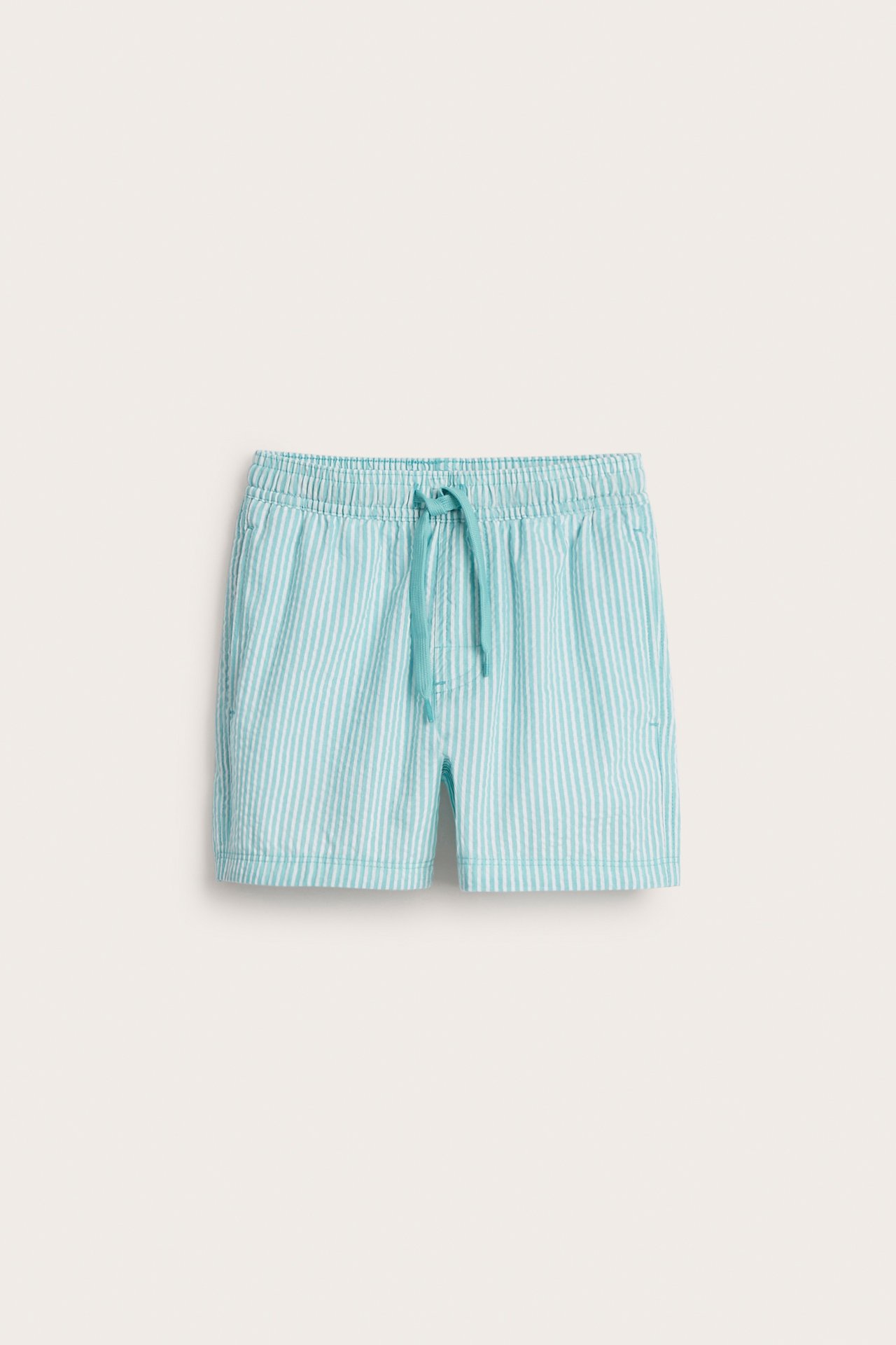 Frontvisning: Stripete badeshorts for barn i turkis og hvit seersucker med elastisk snøring i midjen.