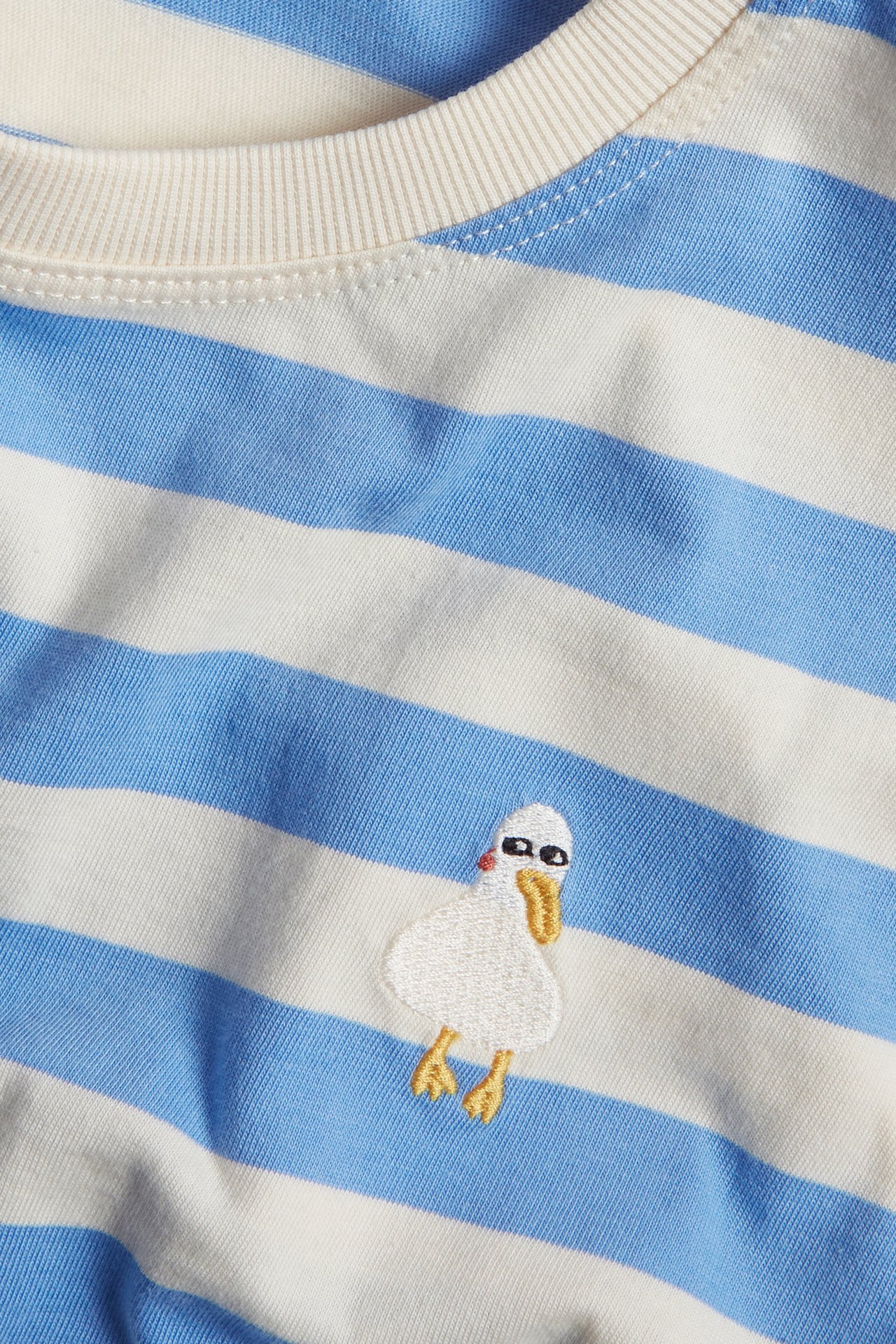 Zbliżenie na bawełniany t-shirt niemowlęcy w niebiesko-białe paski z małą haftowaną kaczką.