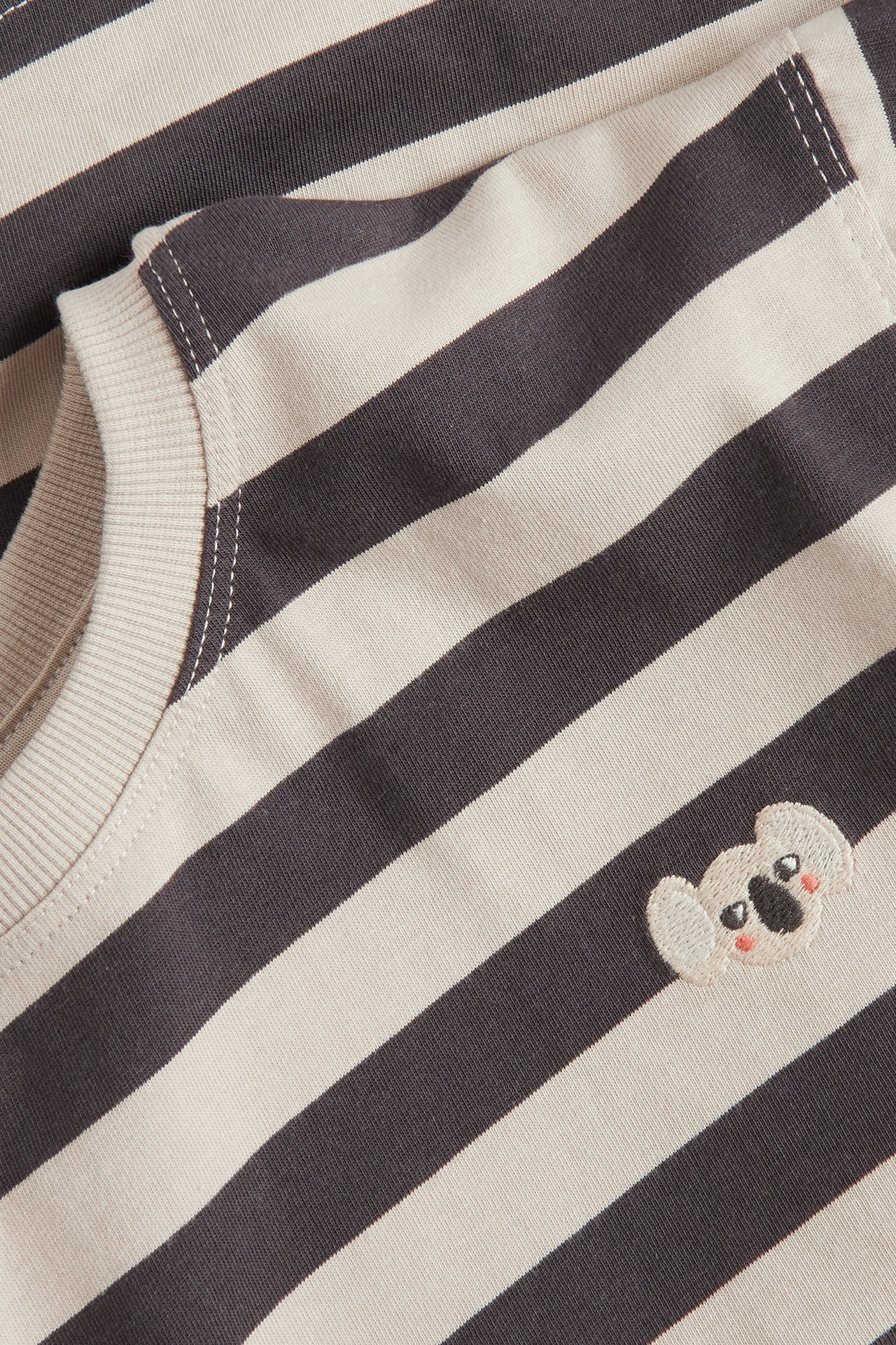 Närbild på en baby-t-shirt i svart och benvit bomull med ränder och en liten broderad koala på bröstet.