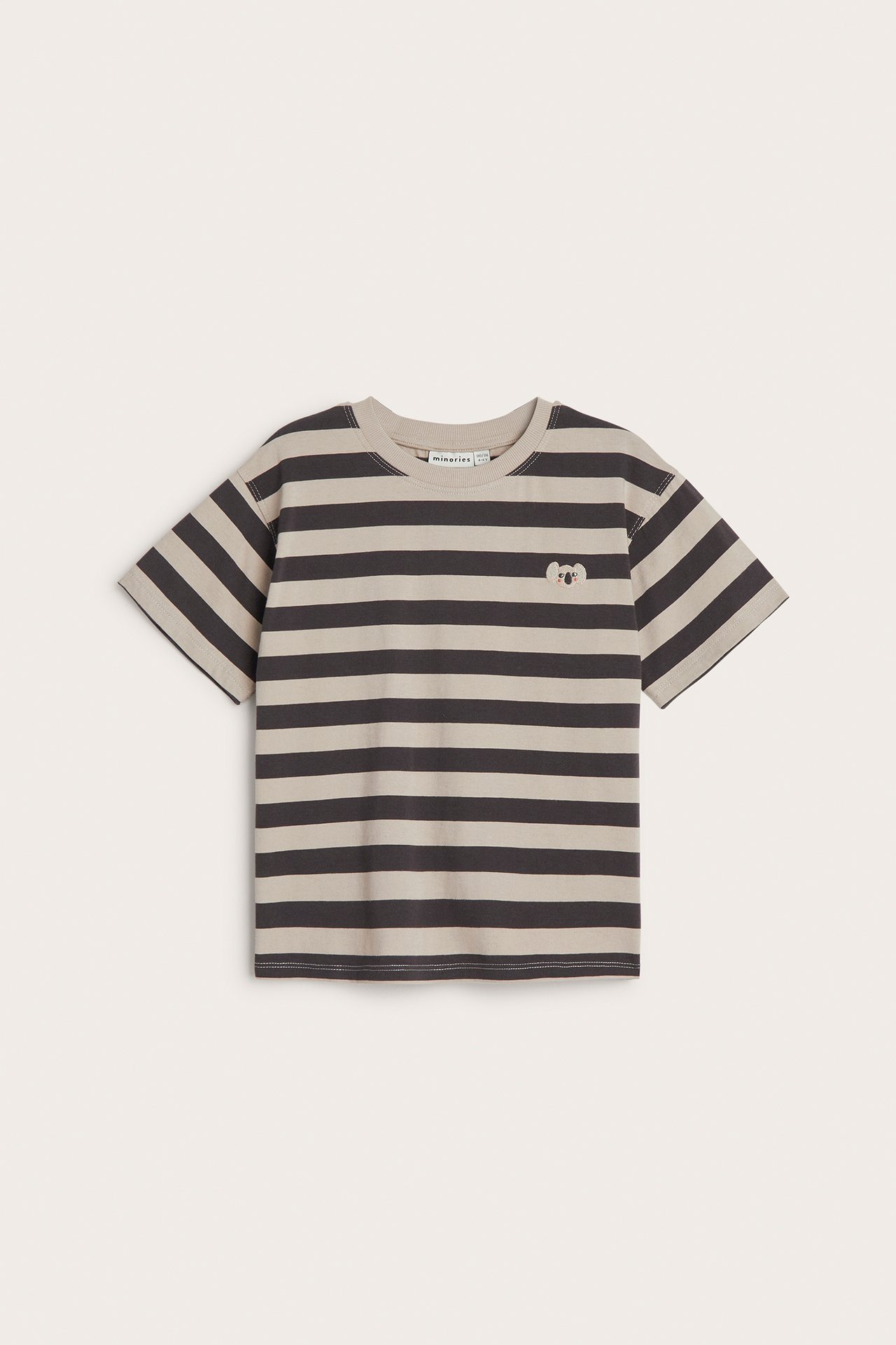 Framifrån, en randig t-shirt i svart och beige bomull för barn, med litet koalabroderi på bröstet.