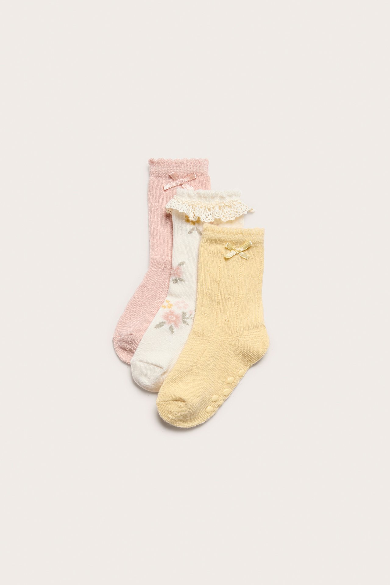 Ovenfra: tre babysokker: rosa, blomstret med blonde, og gul pointelle med antiskli.