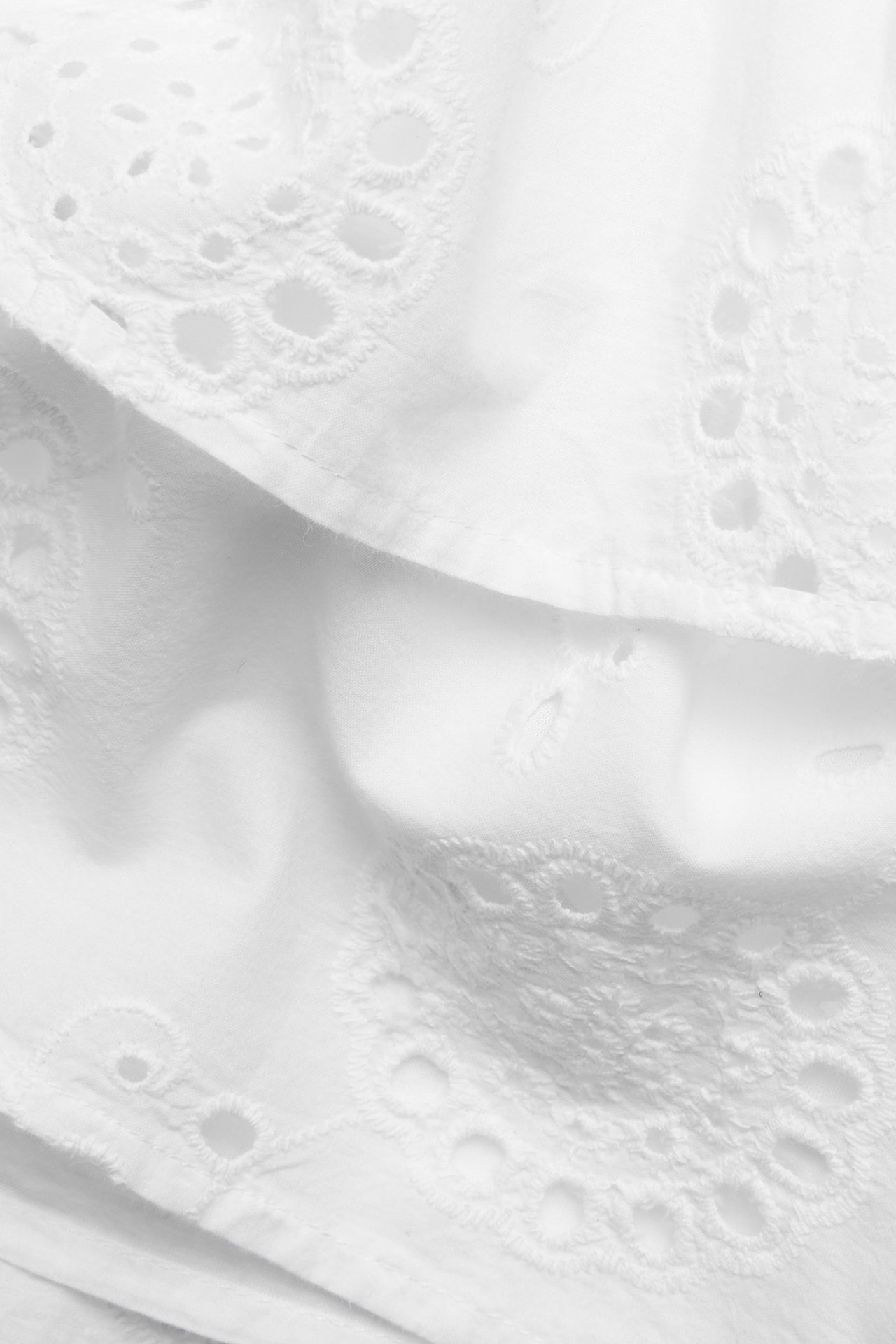 Zbliżenie białej bawełnianej spódnicy z falbanami i haftem angielskim.