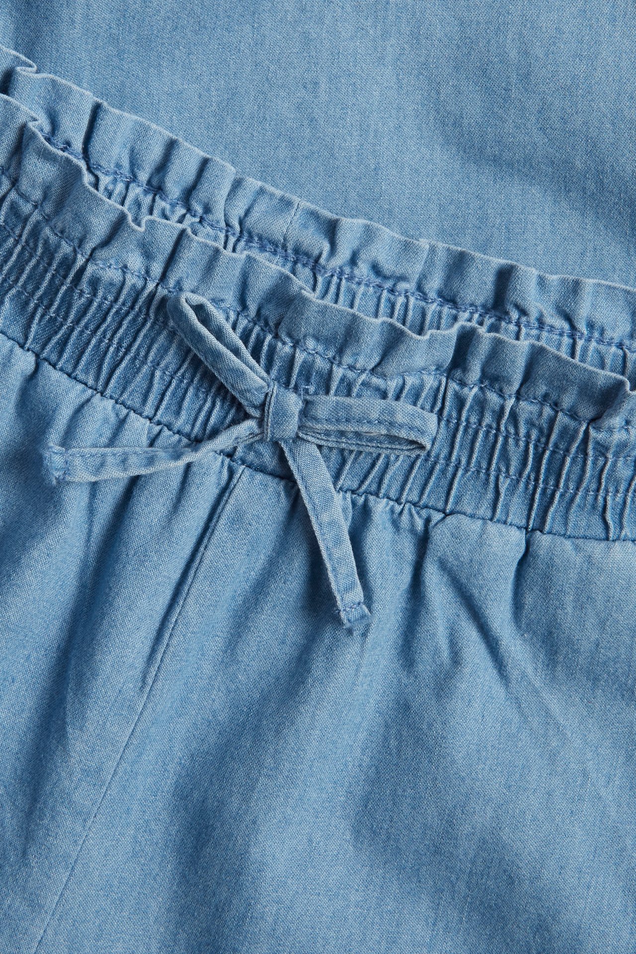 Zbliżenie na jasnoniebieskie dziecięce culotte z denimu z elastyczną talią i ozdobnym sznurkiem.