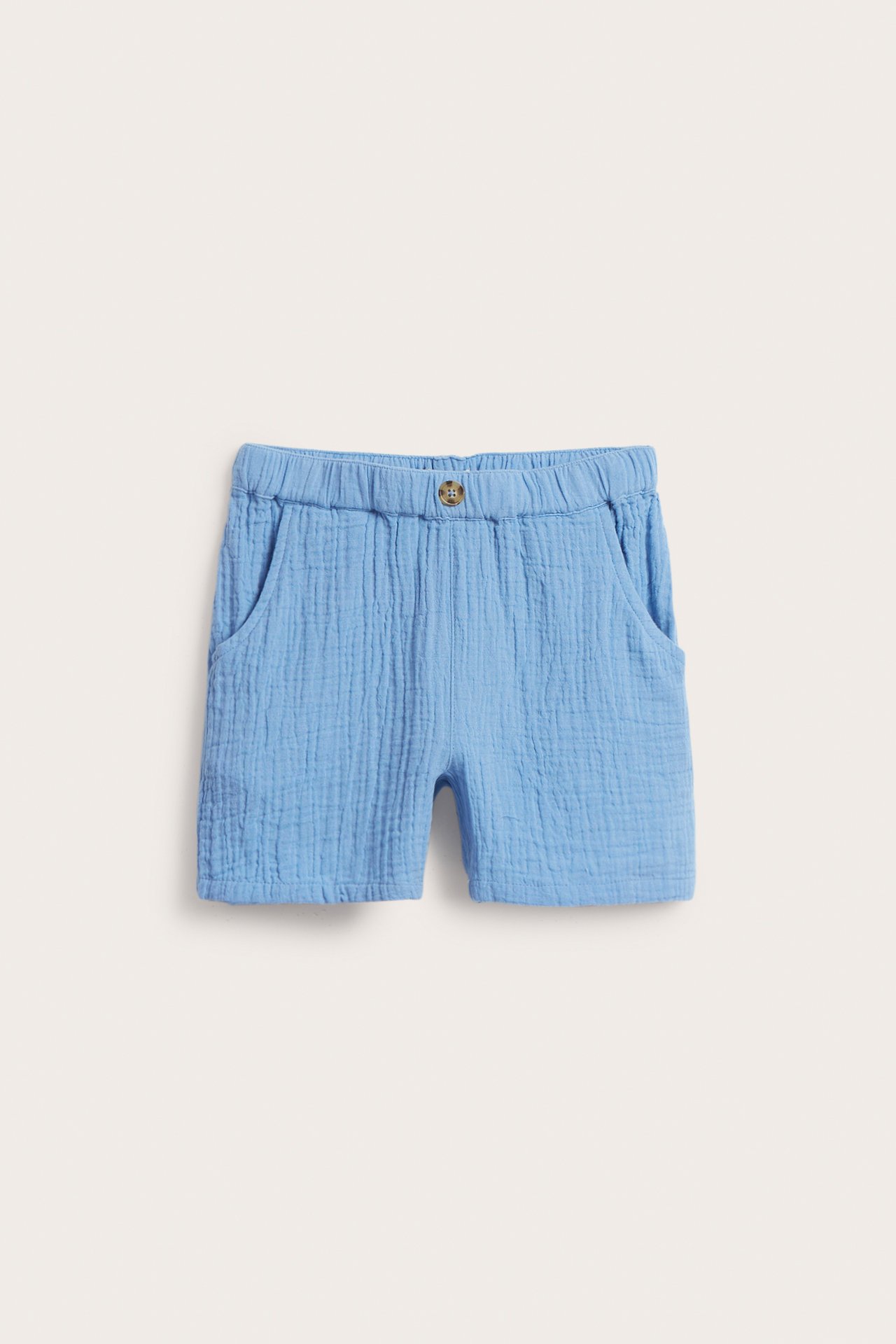 Framifrån, ljusblå shorts i muslin för barn med resår i midjan och en dekorativ knapp.