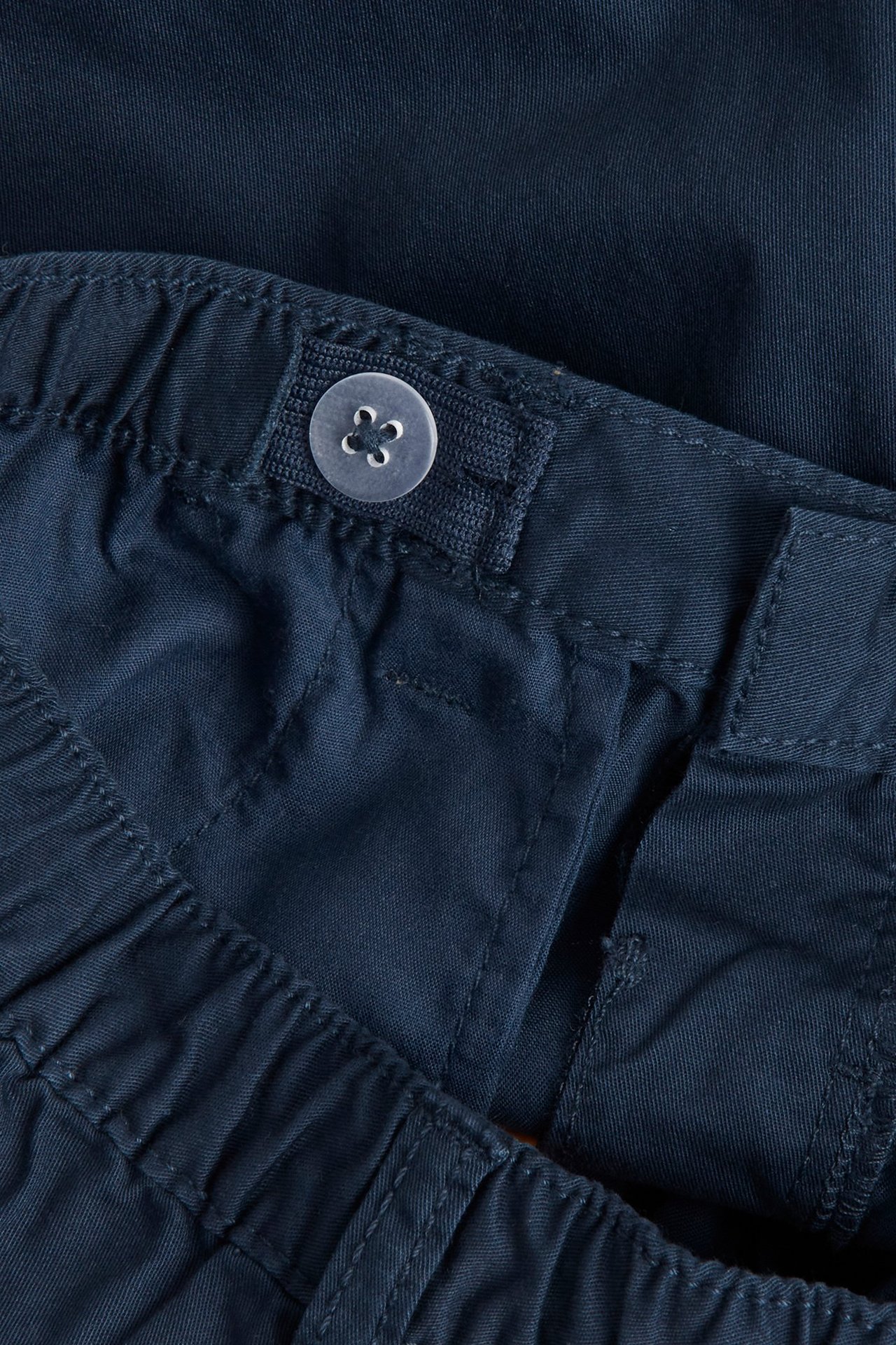 Zbliżenie na granatowe tkane szorty bawełniane dla dzieci z regulowaną elastyczną talią i guzikiem.