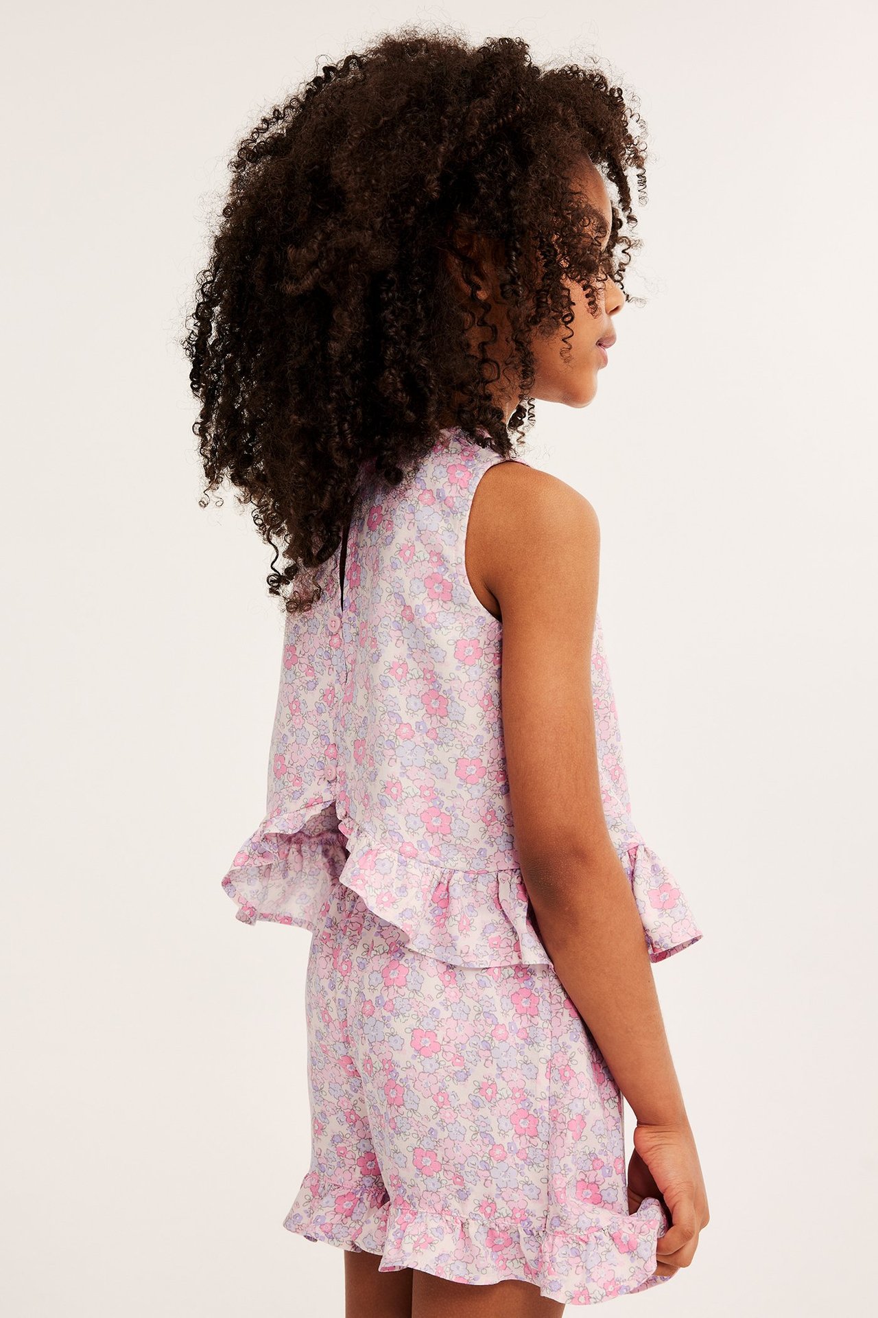 Sidovy av ett barn i en rosa blommig viskosblus med volanger och matchande shorts.