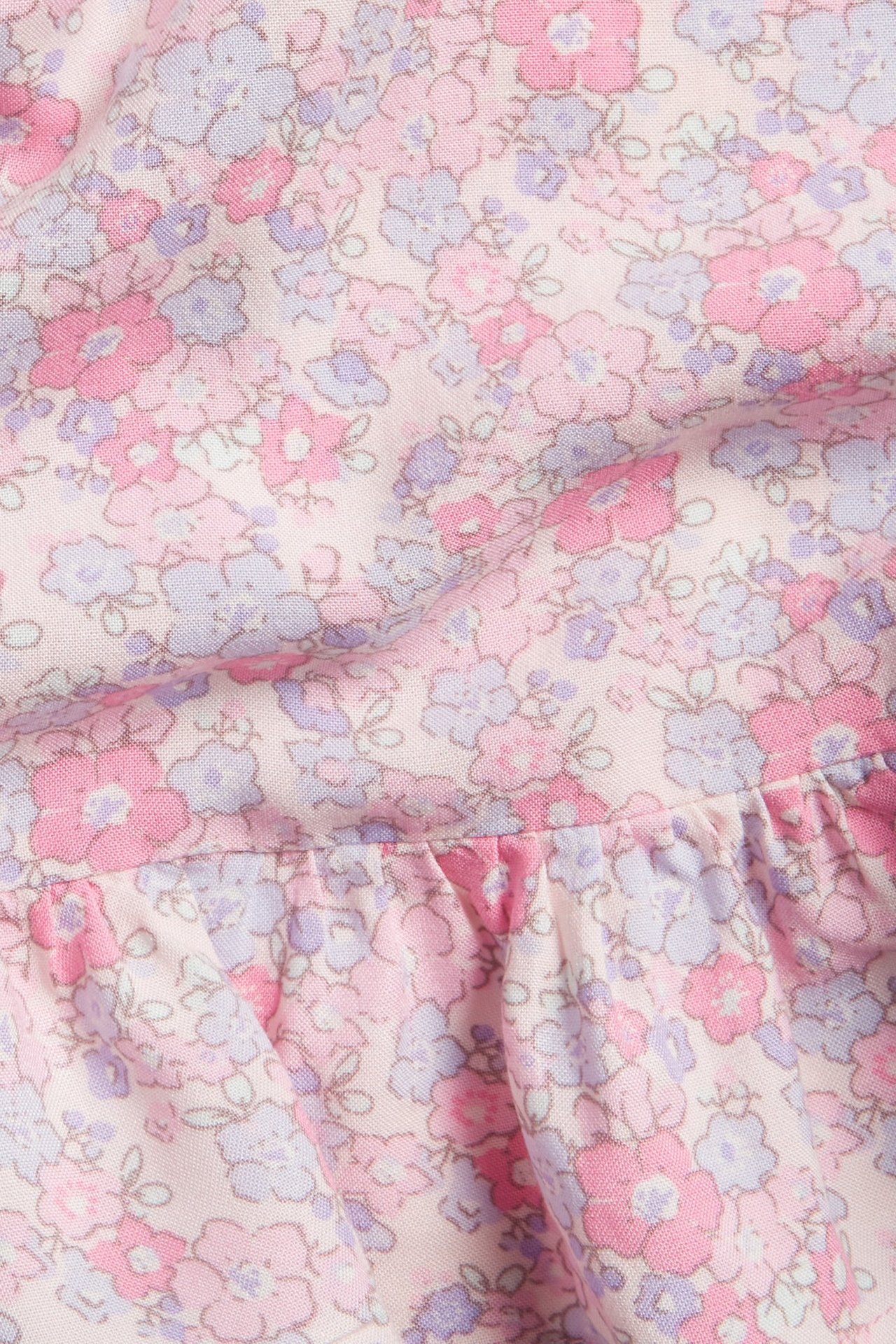 Zbliżenie różowej bluzki wiskozowej z fioletowo-różowym wzorem kwiatowym i falbanką.