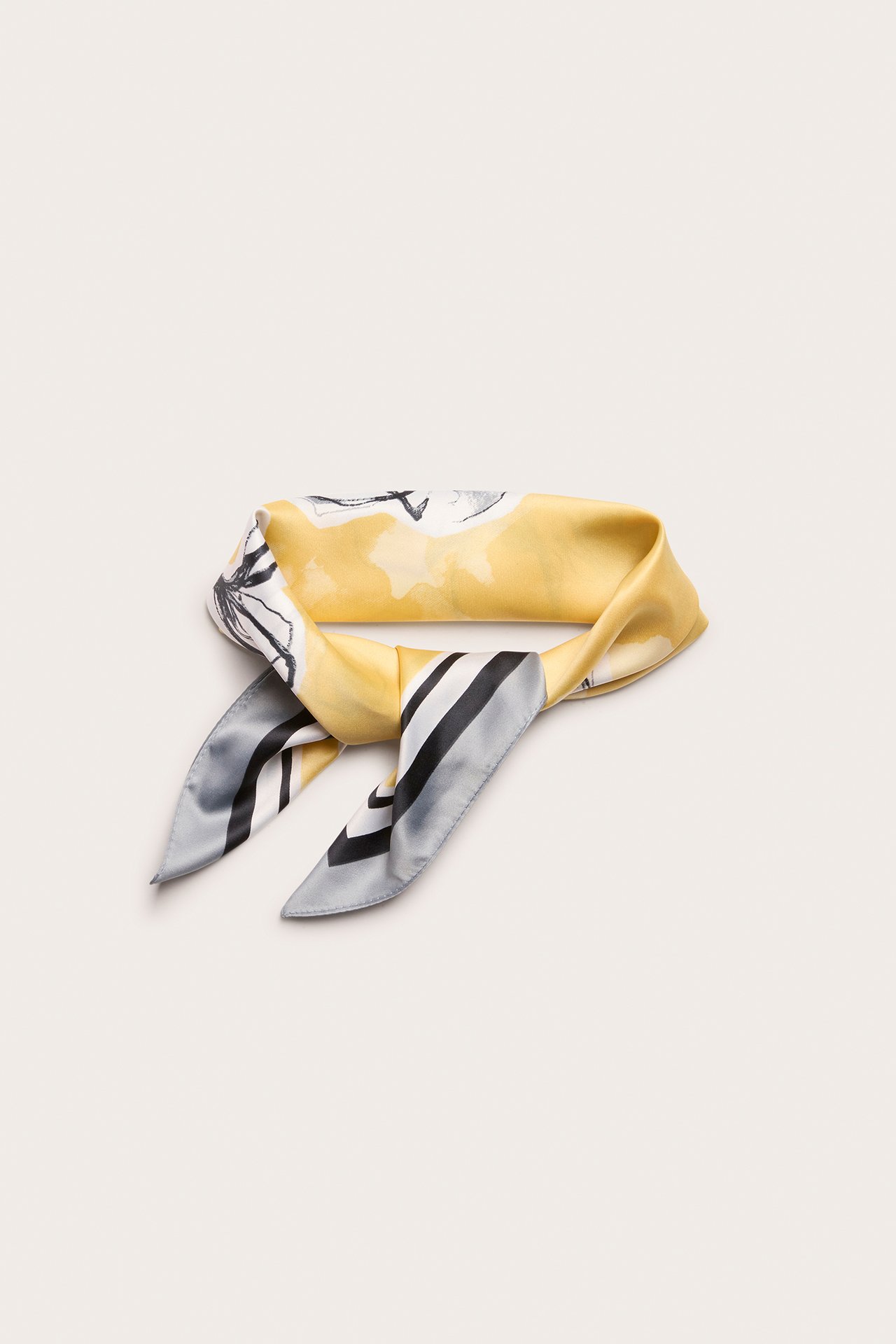 Widok z góry na żółtą wzorzystą satynową apaszkę zawiązaną w supeł.