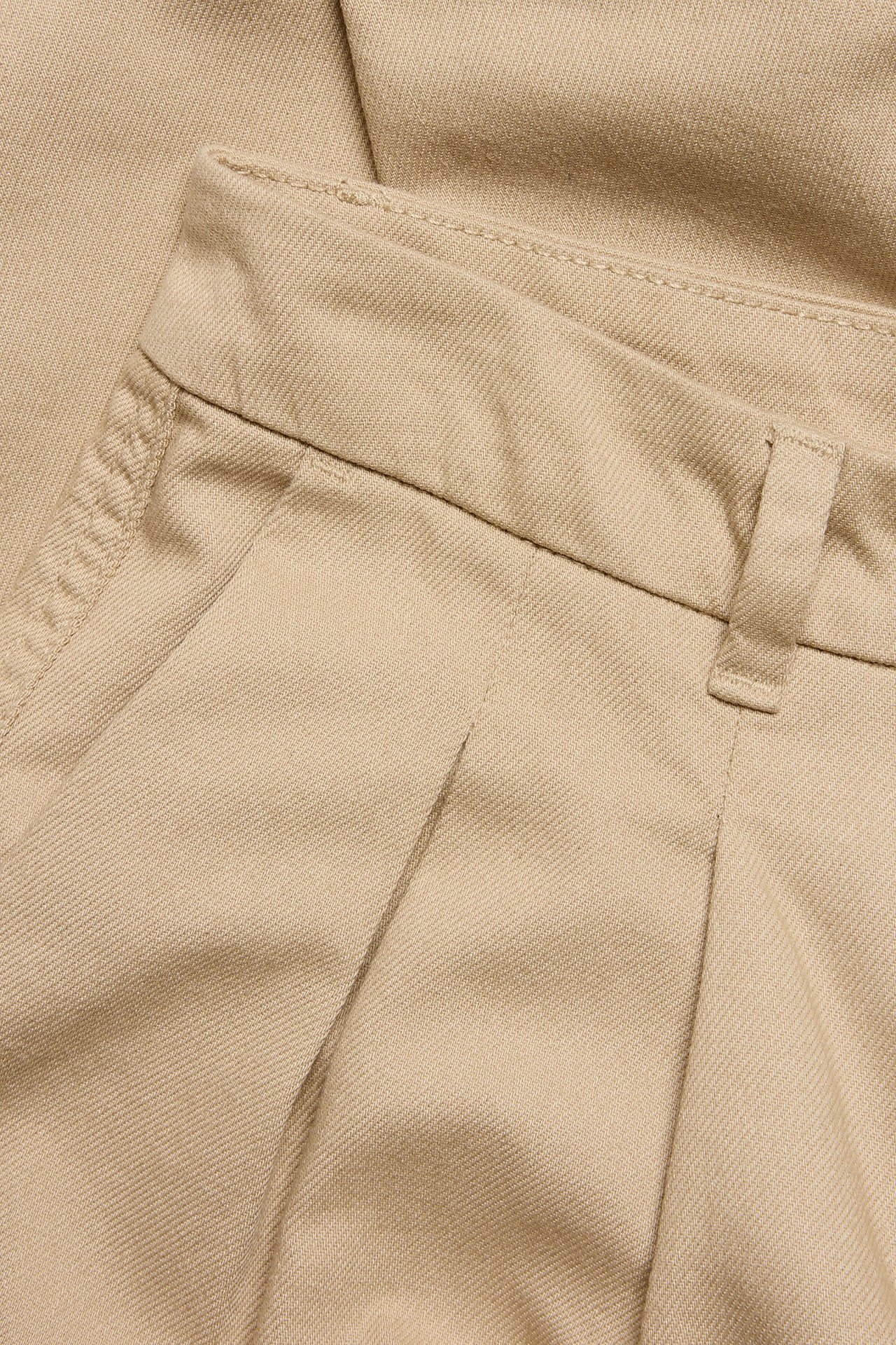 Zbliżenie beżowych bawełnianych spodni capri z zakładkami i szlufkami w pasie.