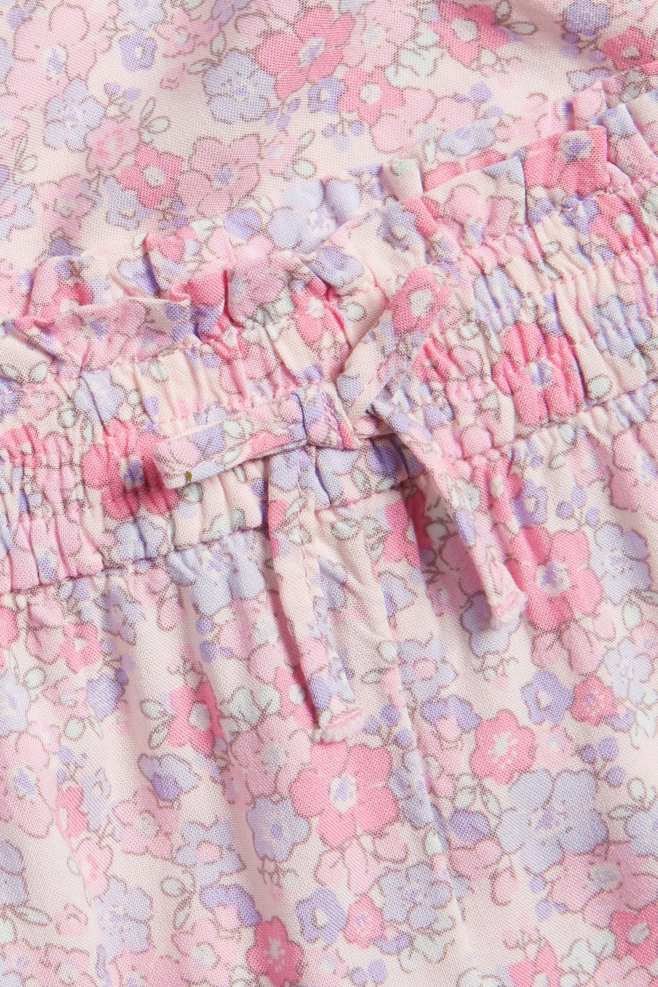 Zbliżenie na różowe, kwieciste spodnie culotte z wiskozy dla dzieci z elastyczną talią i ozdobnym wiązaniem.