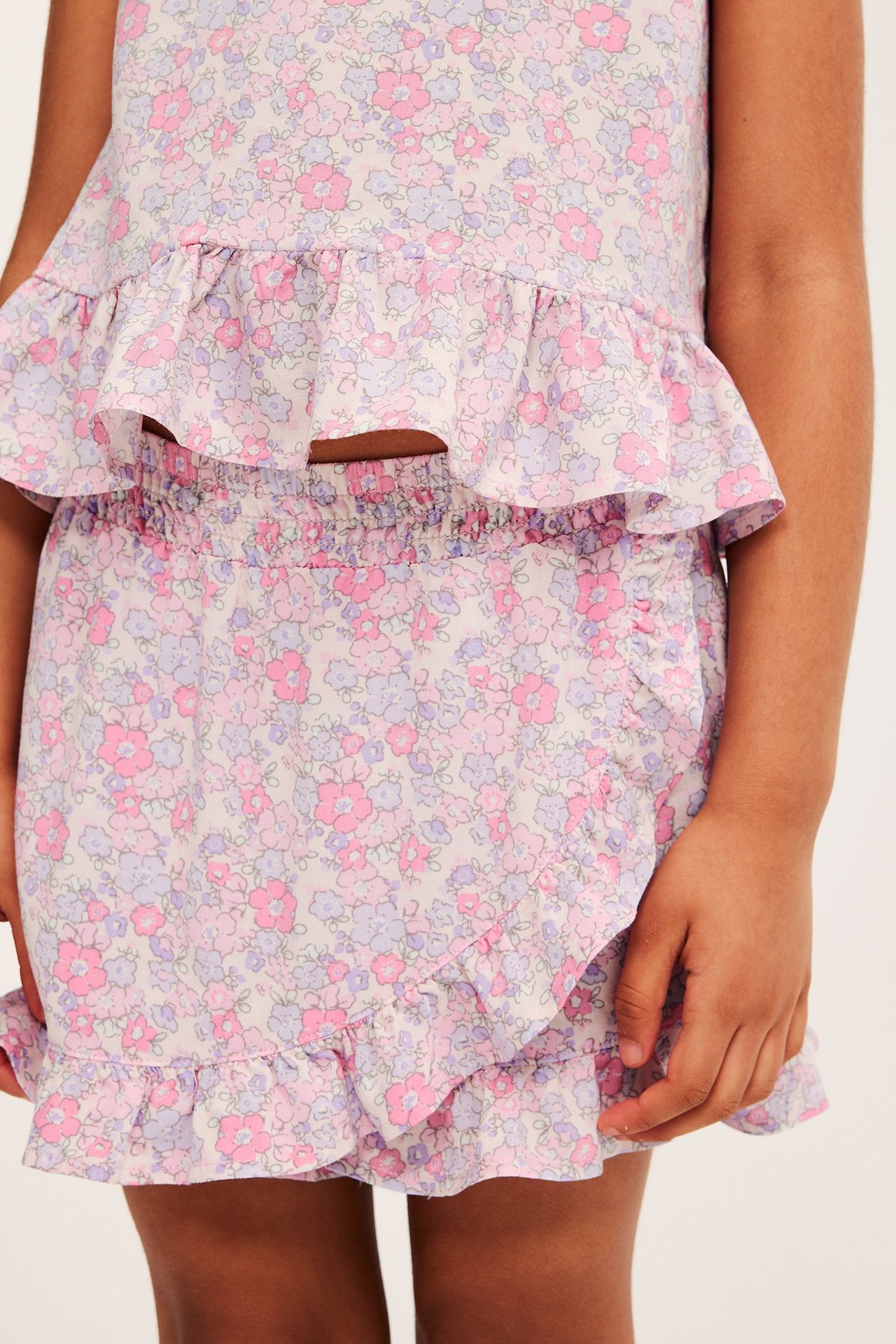 Zbliżenie z przodu dziecka w różowej kwiecistej spódnico-spodenkach z wiskozy z falbankami i pasującym topie.