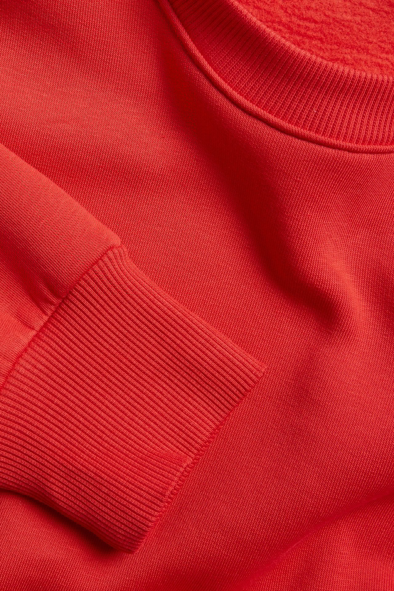 Zbliżenie czerwonej bluzy z mieszanki bawełny z prążkowanym dekoltem i mankietem.