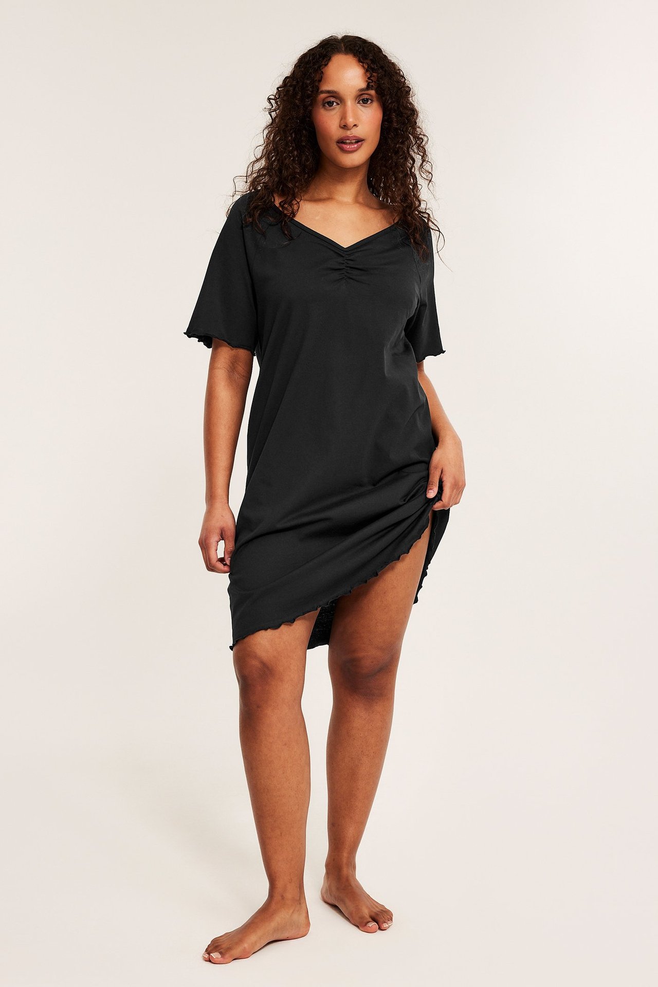 Kobieta przodem w czarnej bawełnianej koszuli nocnej z marszczonym dekoltem w serek i falistymi brzegami.