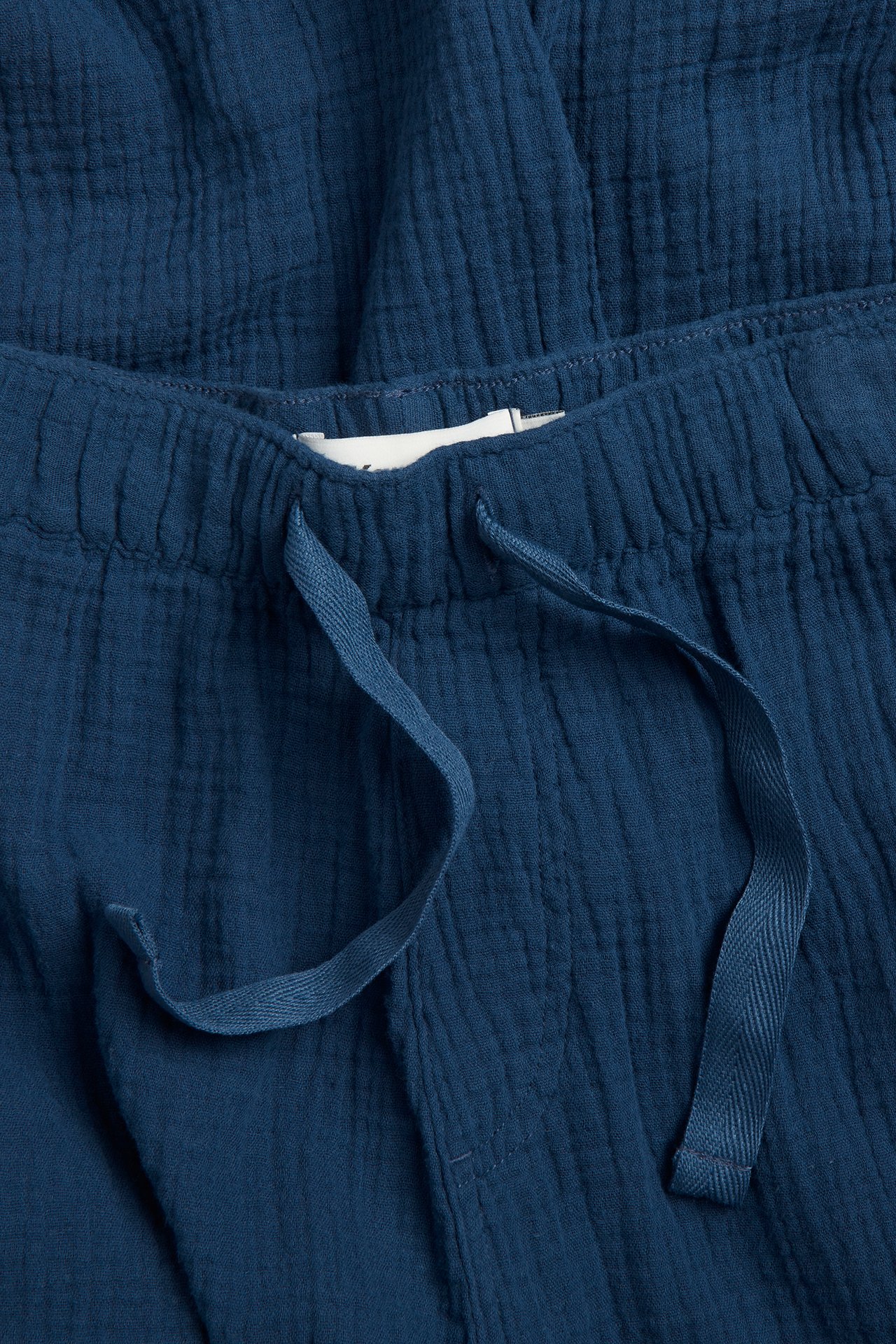 Nærbilde av mørkeblå ensfargede pyjamasbukser i bomullskrepp for menn med elastisk snøring i midjen.