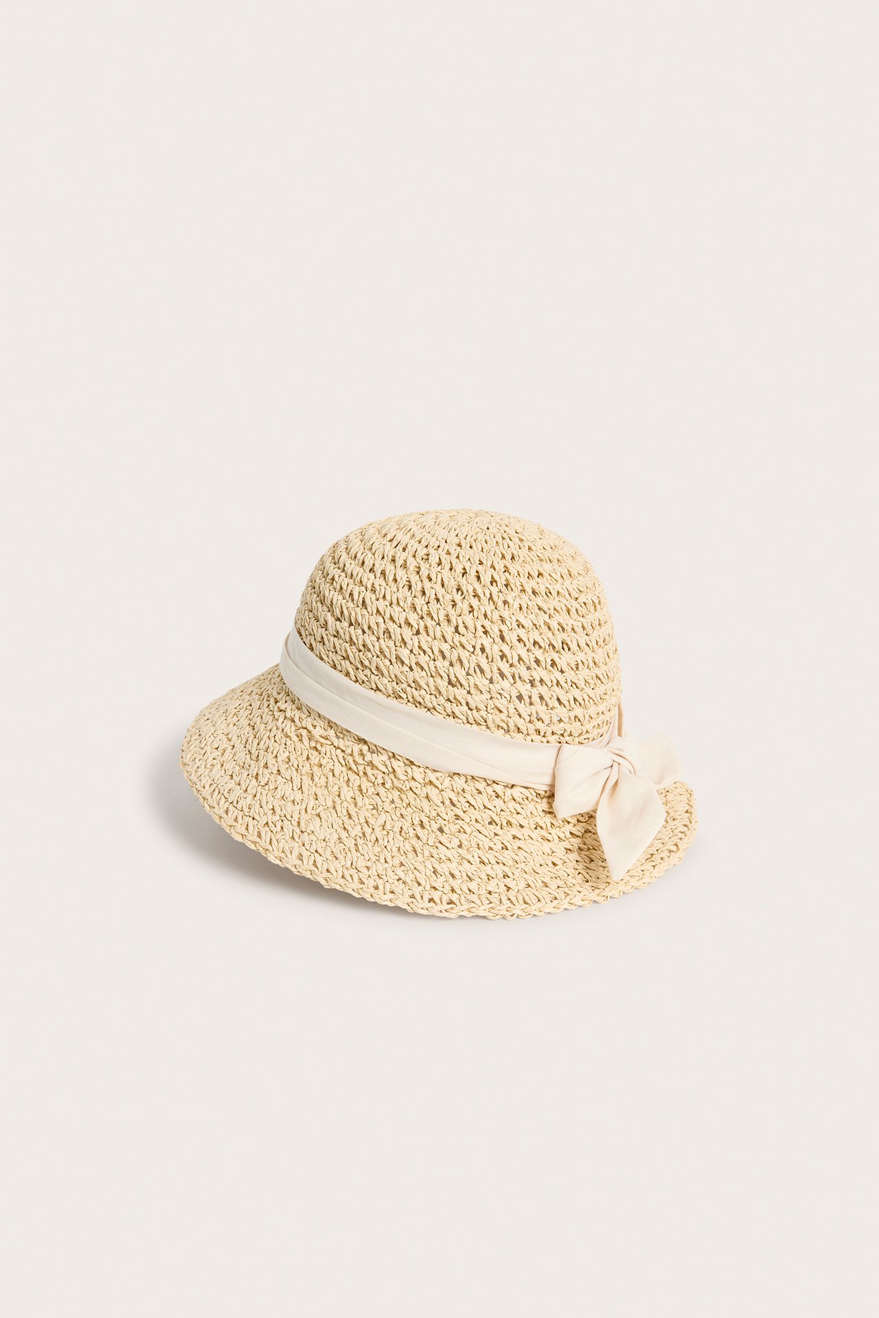 Framsida av en beige vävd stråhatt med klockformad kulle och en krämfärgad rosett.