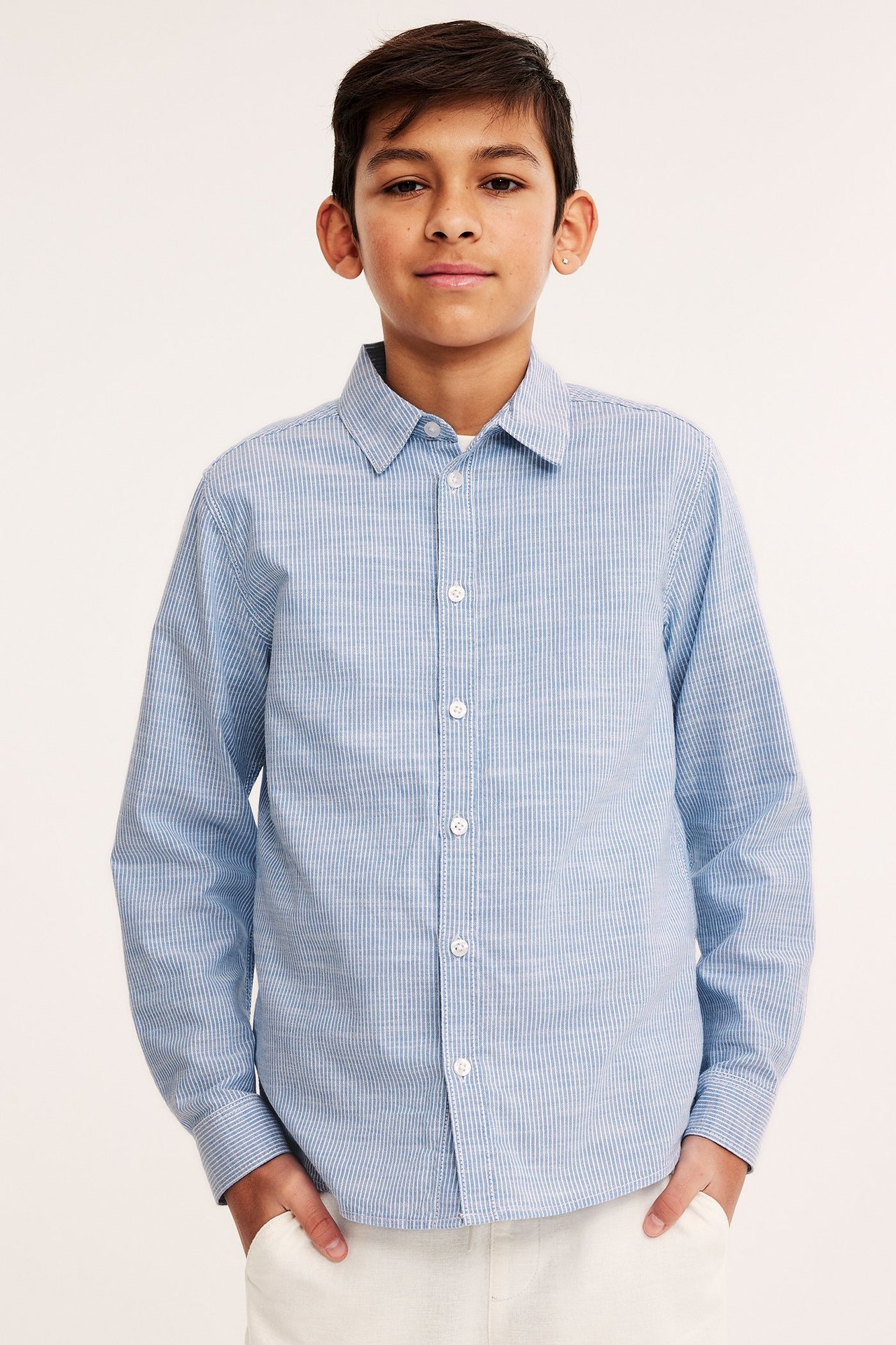 Dziecko z przodu w jasnoniebieskiej bawełnianej koszuli w paski z białymi guzikami i białych spodniach.