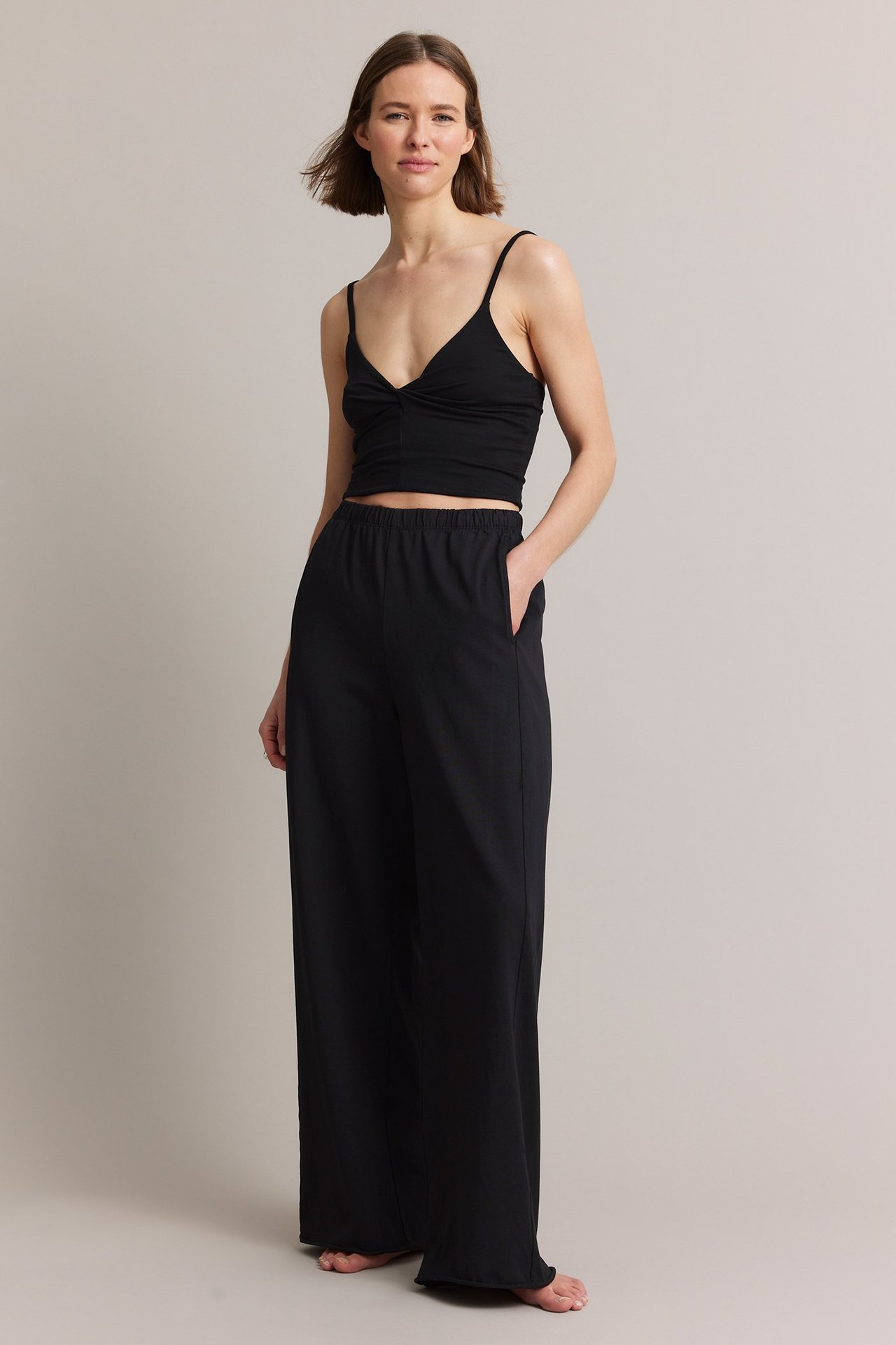 Forfra, kvinne i svarte rette jersey-joggebukser med elastisk midje og sidelommer, samt en svart crop top.