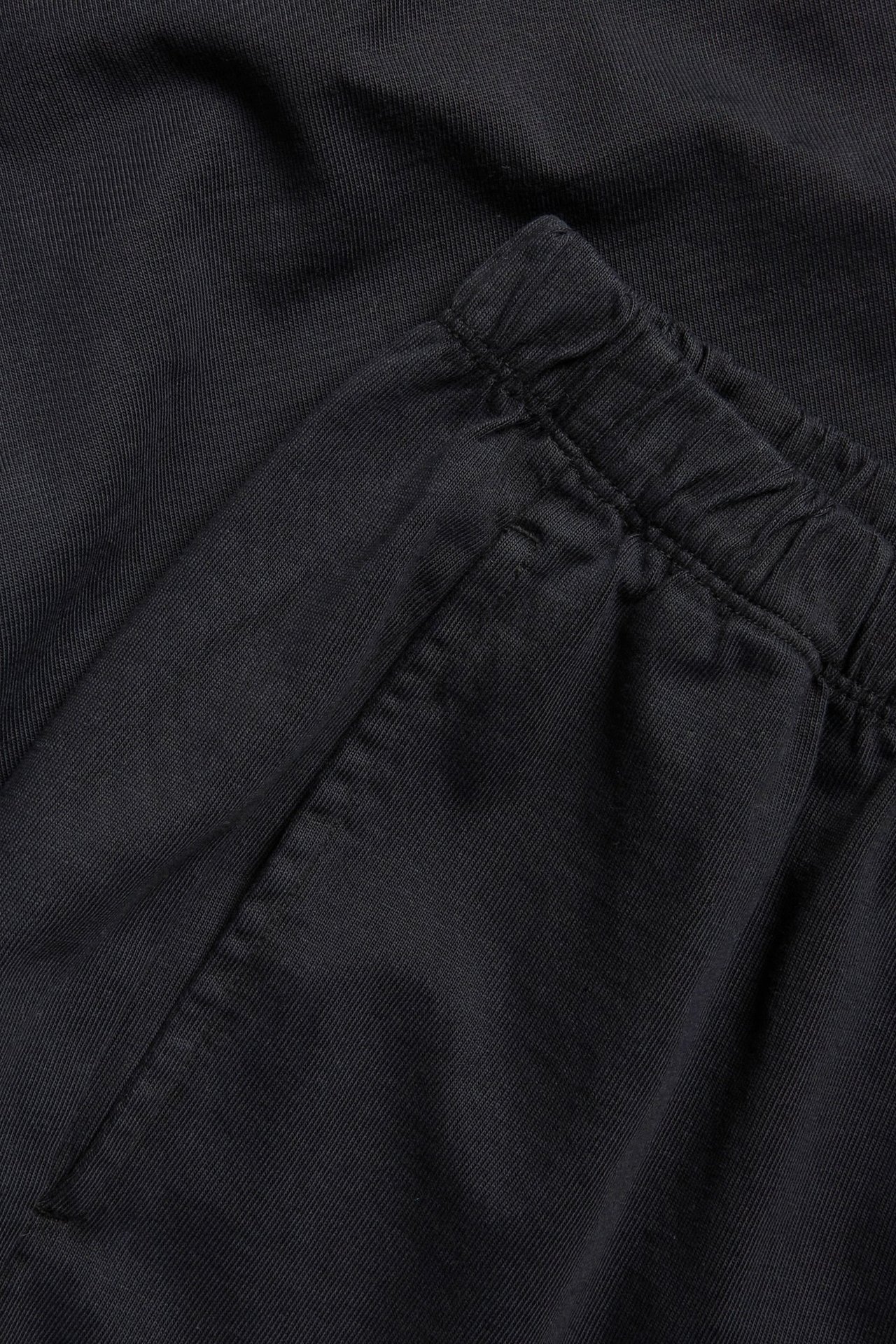 Zbliżenie na czarne proste bawełniane joggery z elastyczną talią i boczną kieszenią.