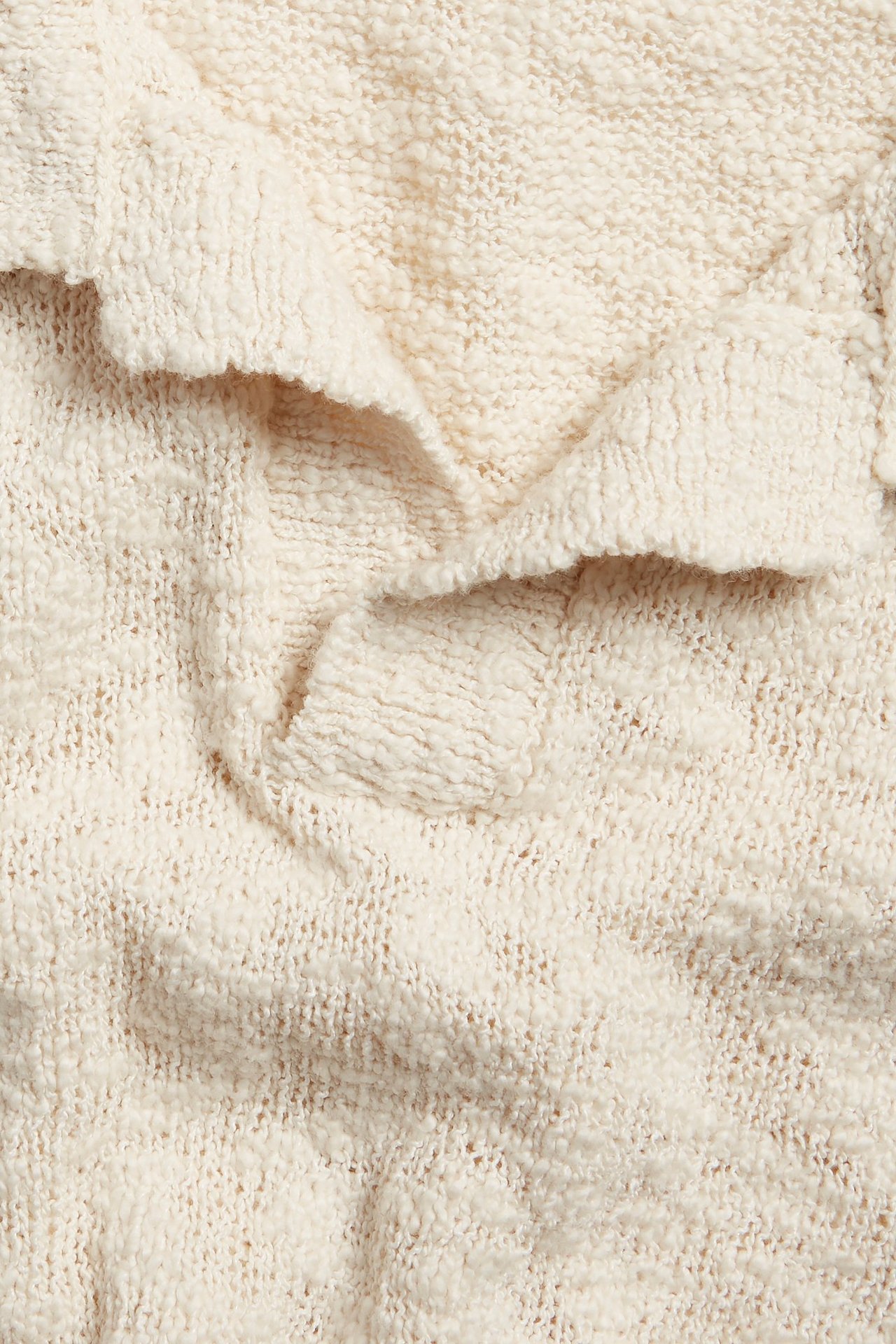 Zbliżenie na ecru, strukturalny dzianinowy materiał krótkiego swetra z widocznym wzorem.