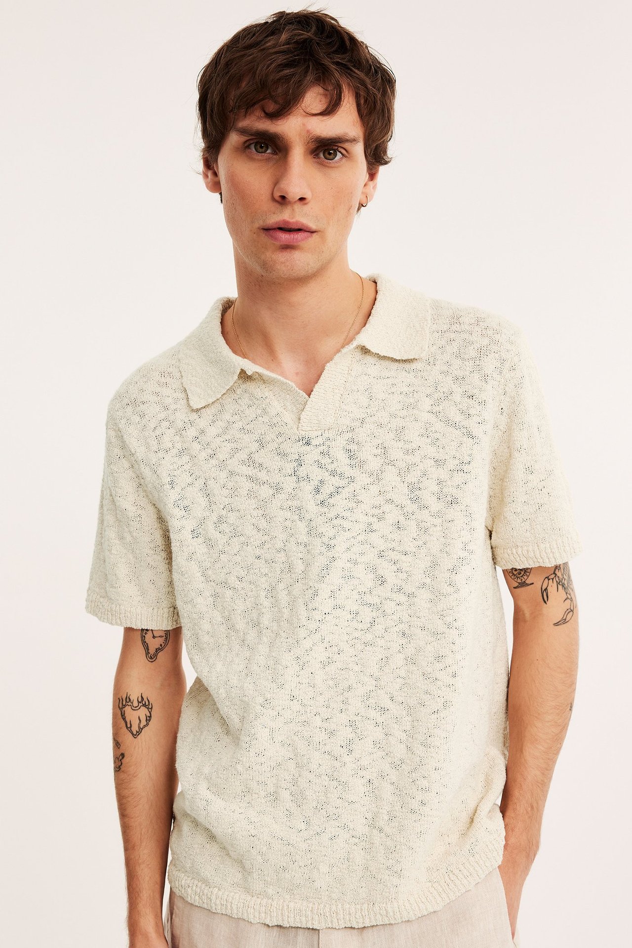 Edestä, mies yllään luonnonvalkoinen strukturoitu neulottu lyhythihainen poolopaita ja vaaleanbeiget housut.
