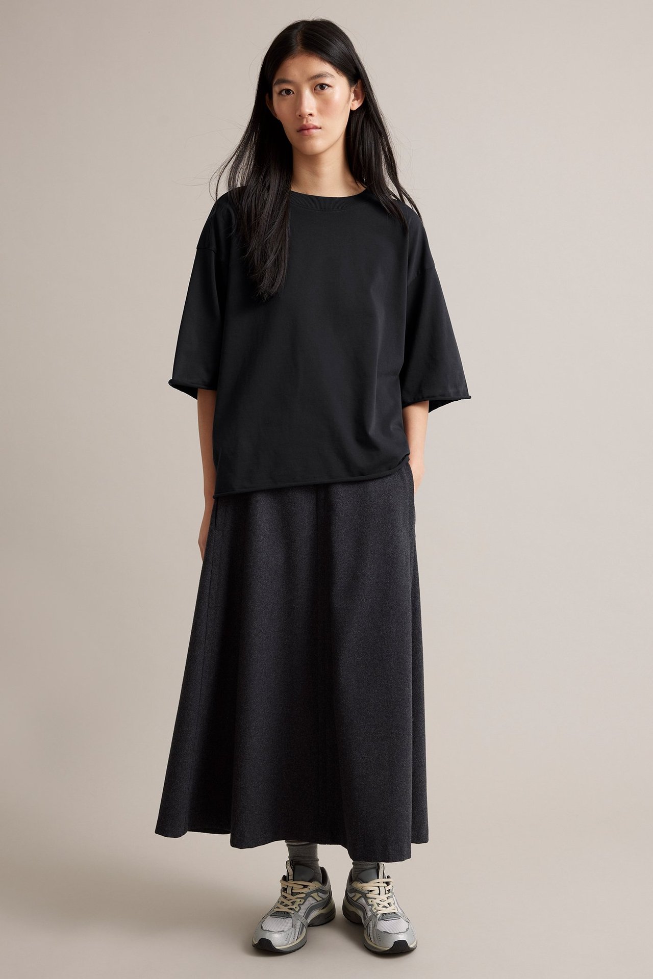 Front: Kvinna i svart bomulls-T-shirt, mörkgrå maxikjol och grå sneakers.