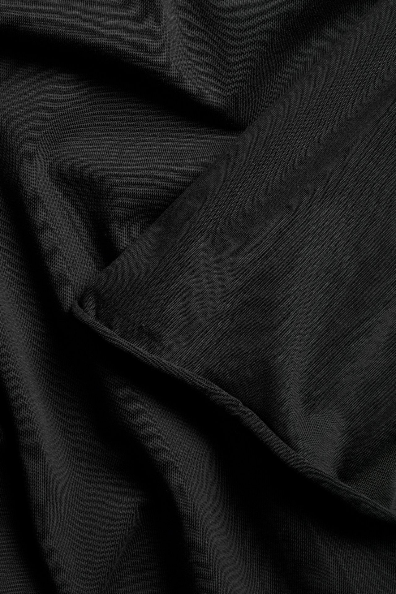 Zbliżenie na czarną bawełnianą tkaninę T-shirtu z widoczną podwiniętą krawędzią i teksturą.