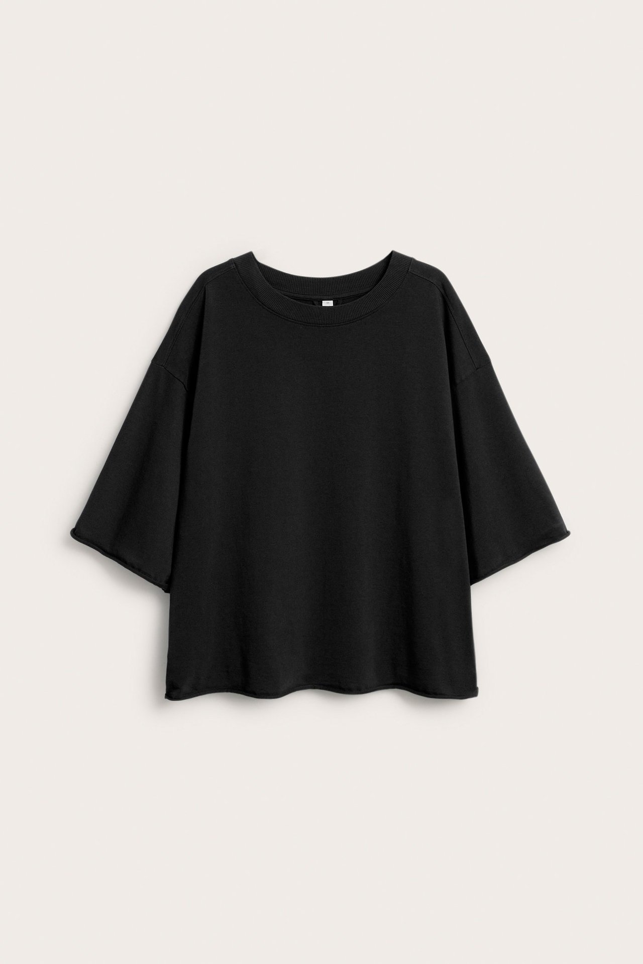 Svart T-shirt i grov trikåkvalitet, tvättad look och råa fållar, kvinnlig modell frontal.