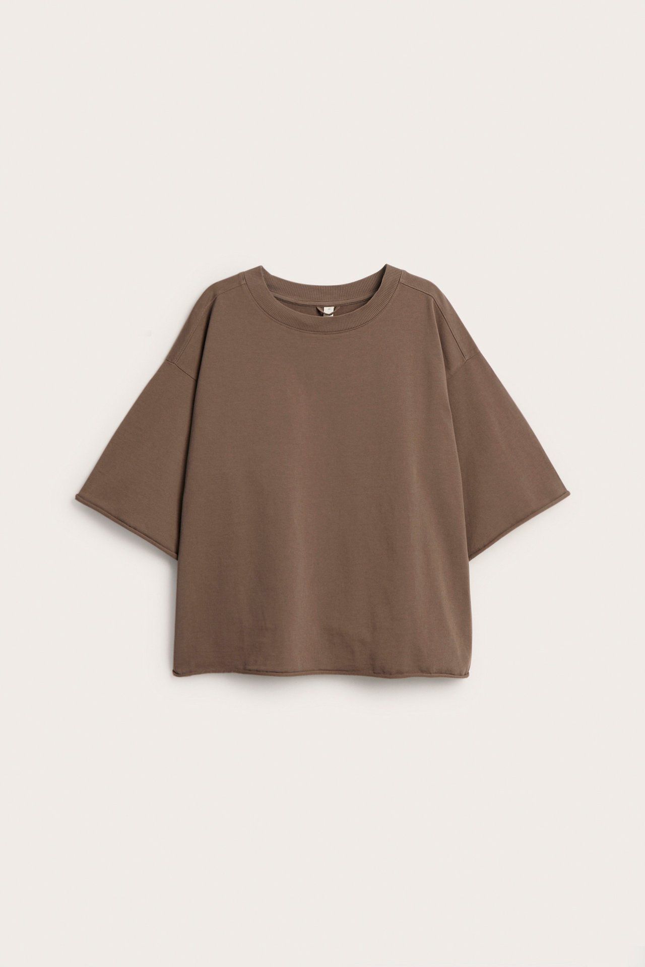 Frontvy av en lös brun bomulls-t-shirt med korta ärmar, rund hals och råa fållar.
