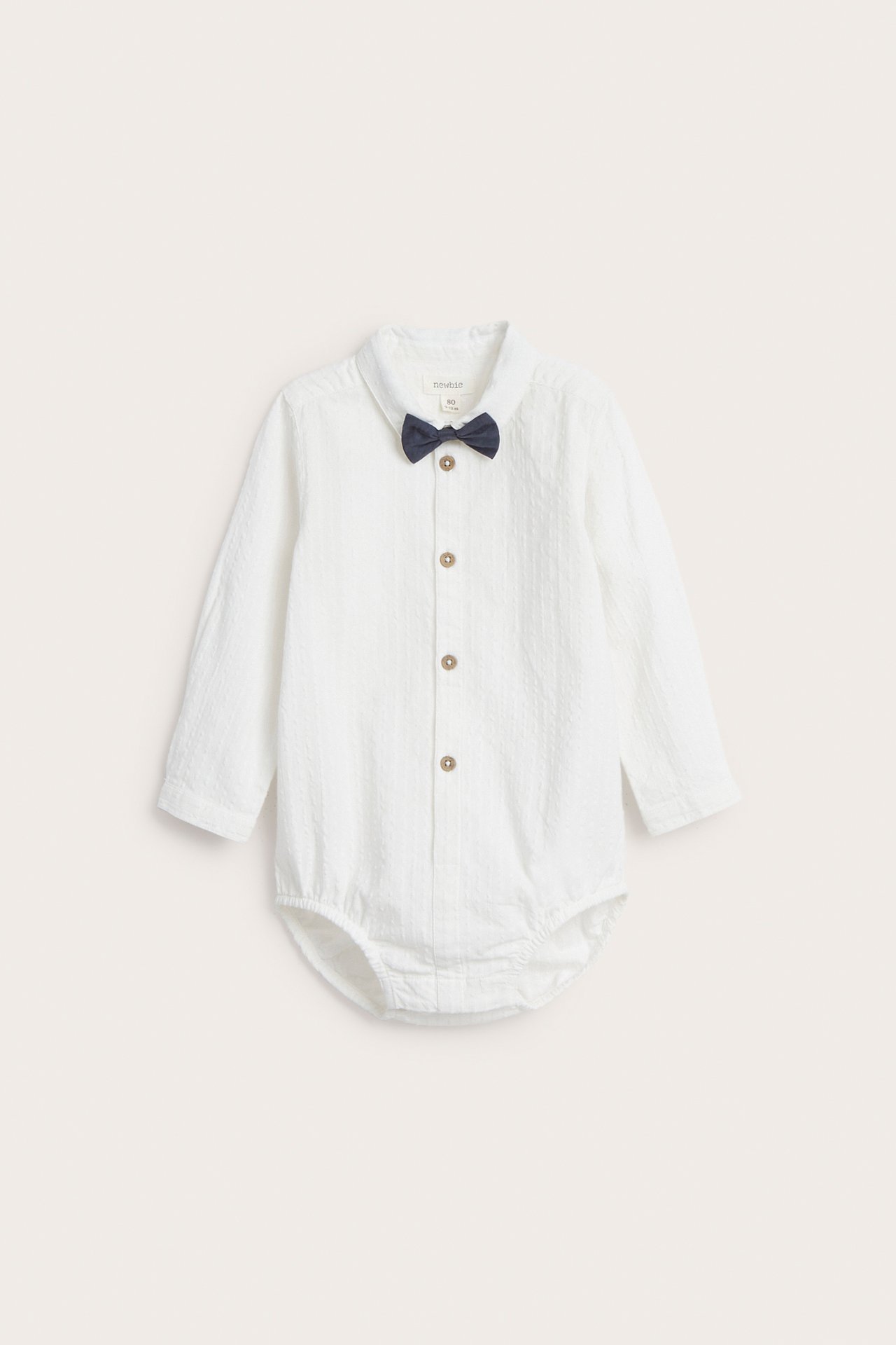 Frontvy av en baby offwhite vävd skjortbody med krage, långa ärmar och en mörkblå fluga.