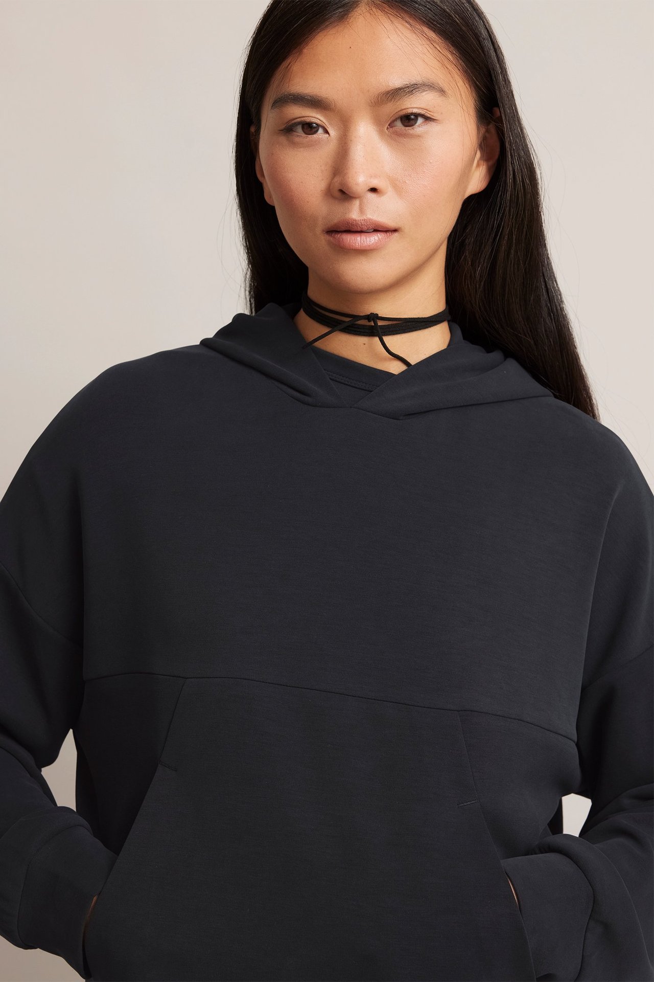 Edestä: nainen mustassa modaalisekoitehupparissa, jossa on kengurutasku ja musta choker.