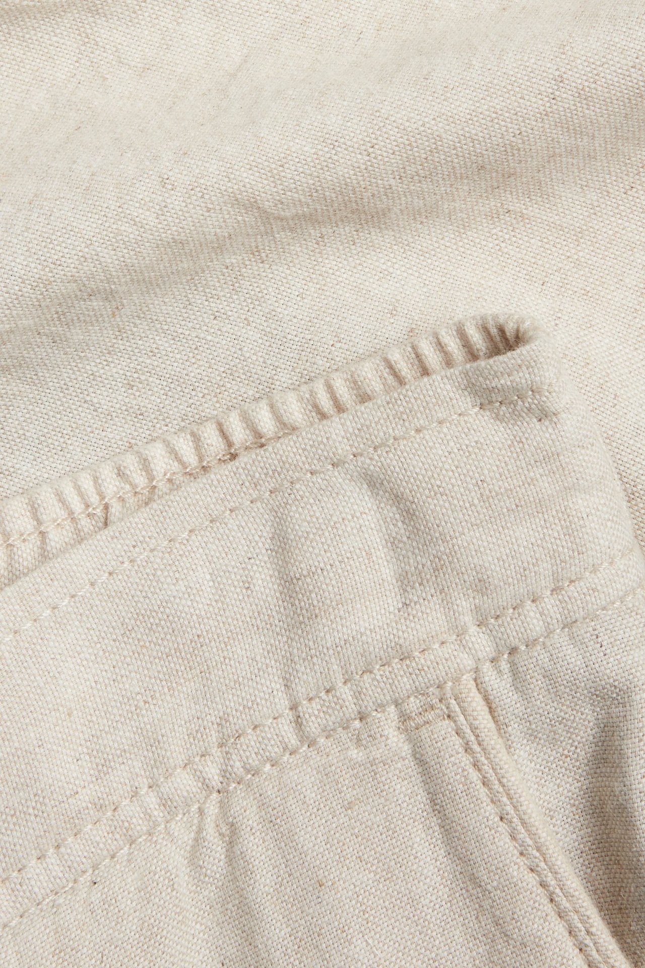 Zbliżenie beżowych szortów z mieszanki lnu, ukazujące teksturę tkaniny i detale szwów.