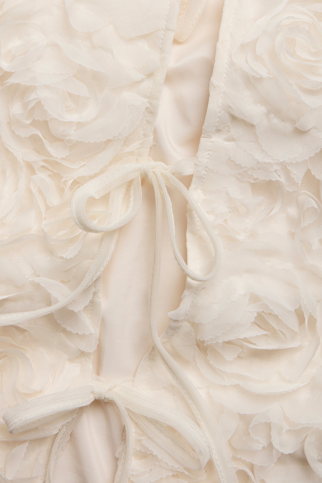 Närbild av en offwhite blus med knytning fram och texturerat blommönster.