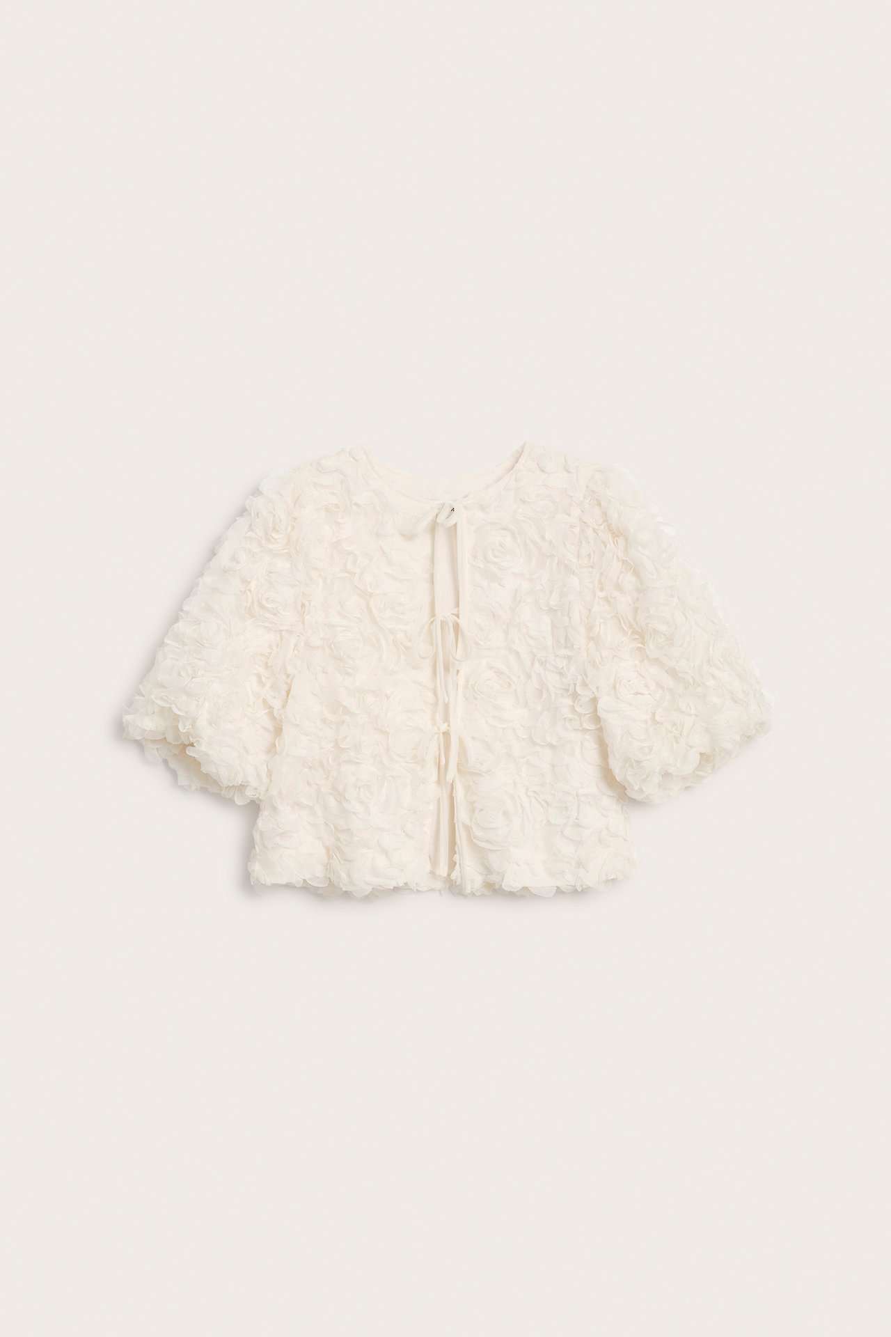 Framifrån: Offwhite blus med puffärmar, texturerat rosmönster och knytband.