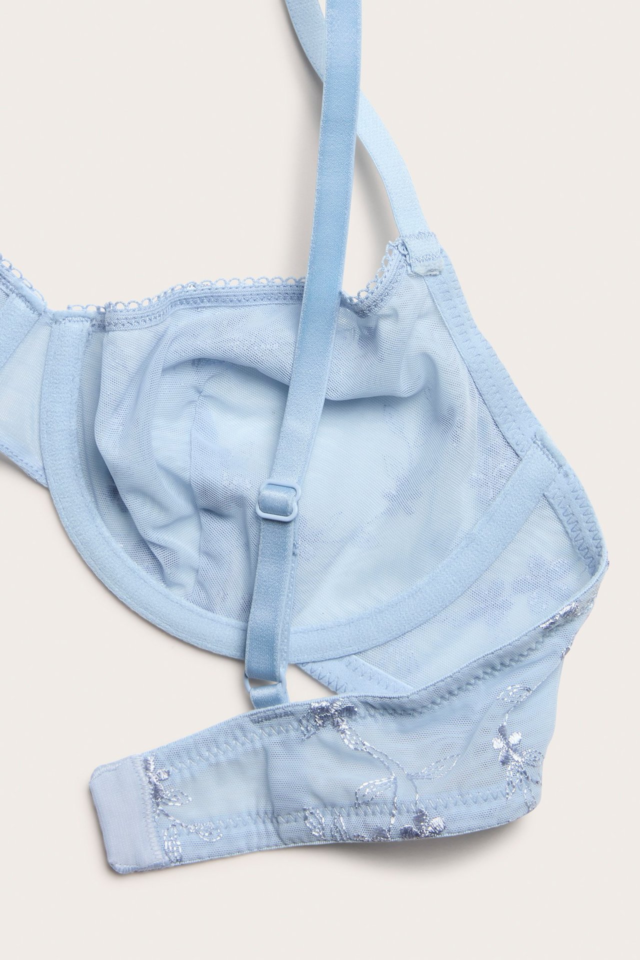 Zbliżenie jasnoniebieskiego biustonosza z fiszbinami, z siateczki, z haftem i regulowanymi ramiączkami.
