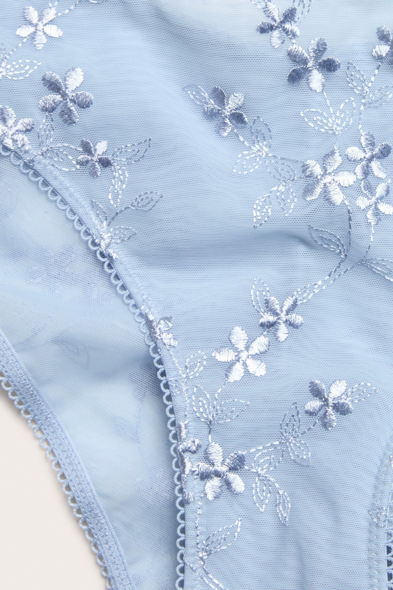 Zbliżenie na jasnoniebieskie koronkowe figi brazilian z białym haftem kwiatowym.