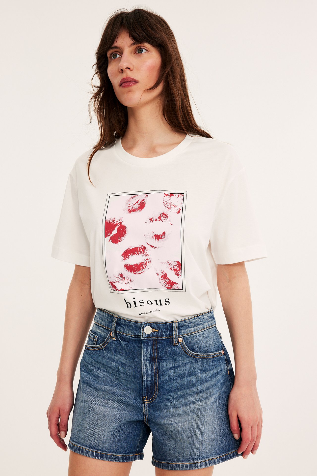 Widok z przodu kobiety w niebieskich szortach jeansowych i białym T-shircie z czerwonym nadrukiem ust.