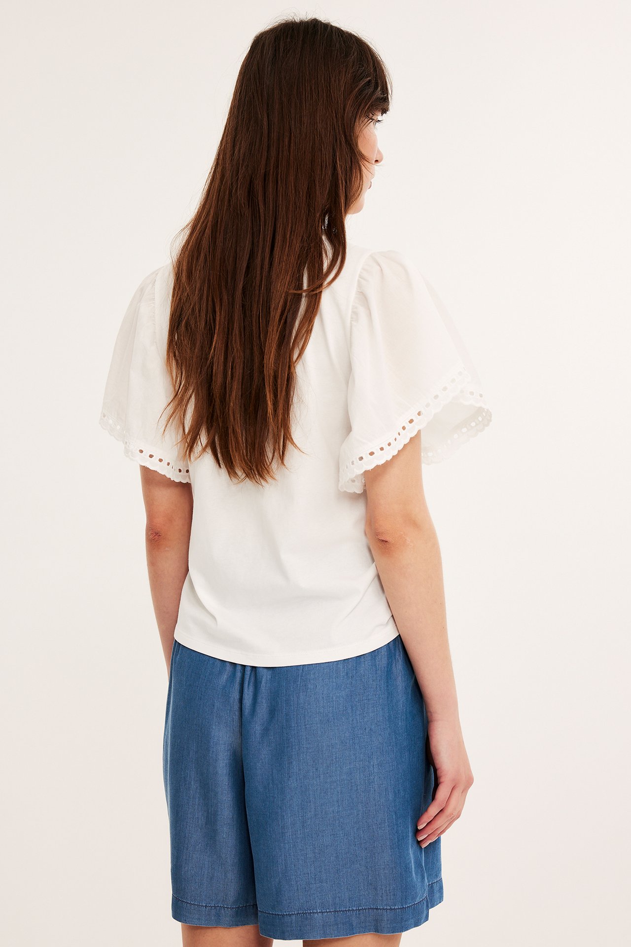 Bakfra av en kvinne i blå Tencel-shorts med smock i midjen og en hvit kortermet topp.