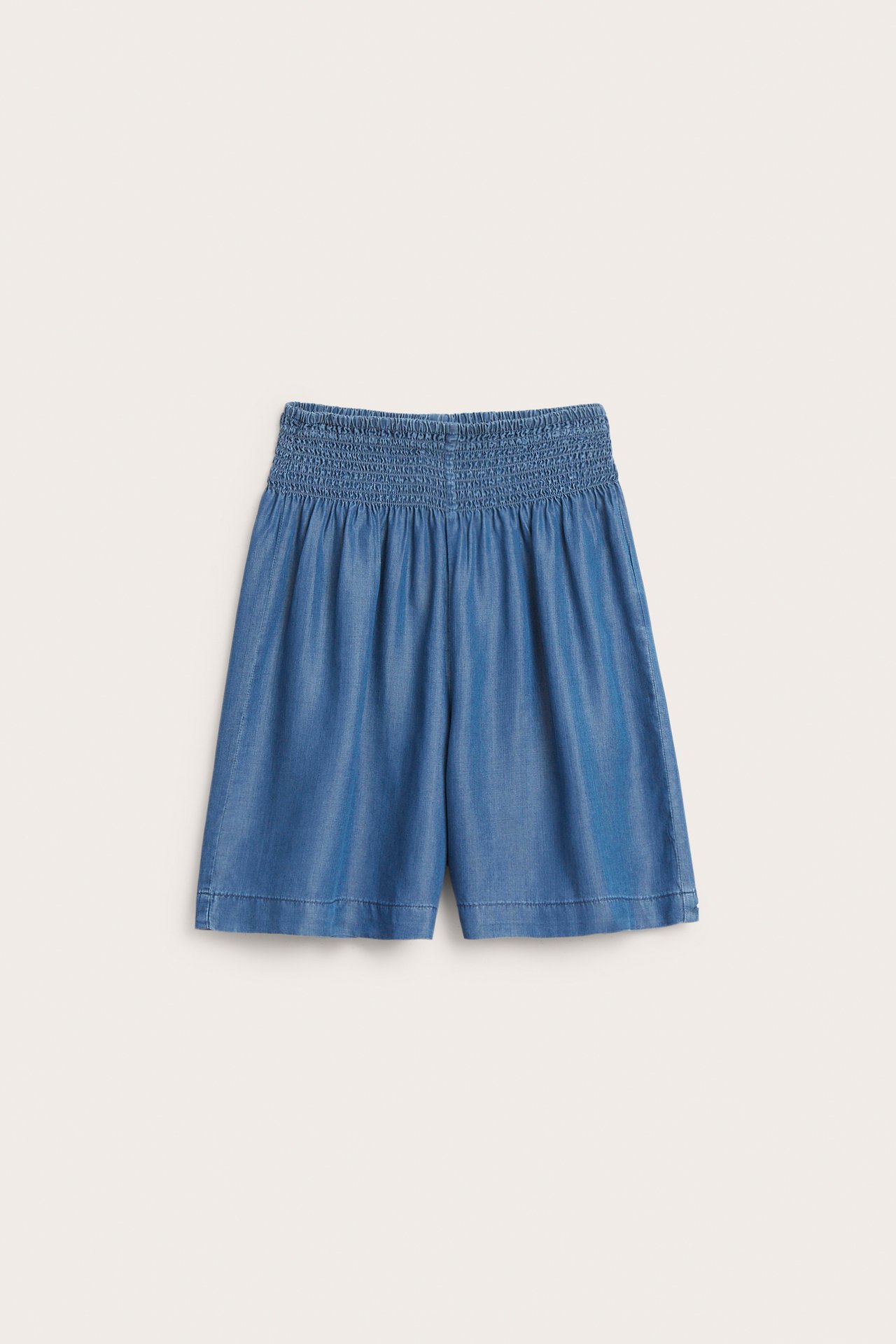 Frontvisning av blå Tencel-shorts med smock i midjen og vide ben.