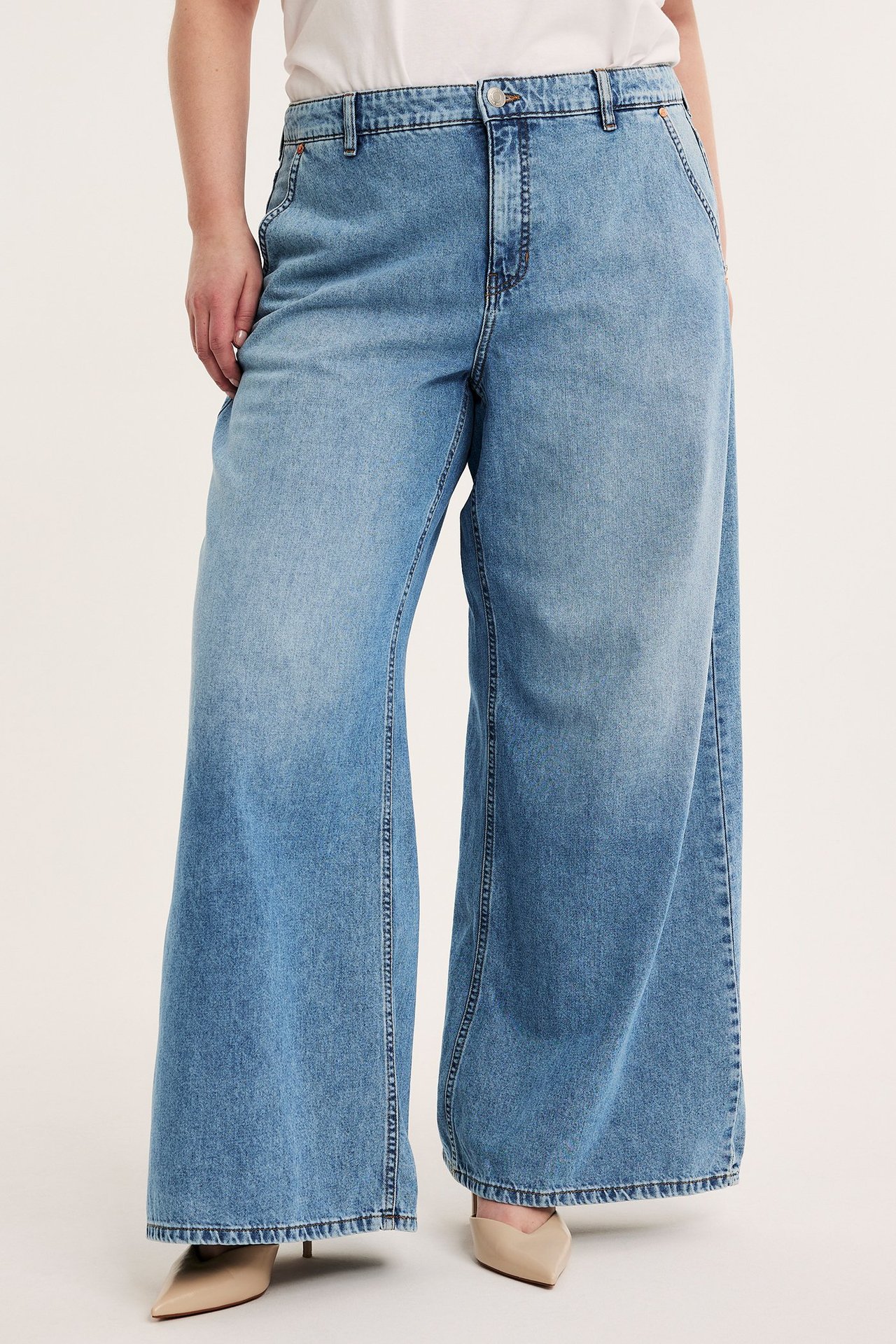 Framifrån: kvinna i ljusblå vida jeans med hög midja, vit t-shirt och beiga spetsiga klackskor.