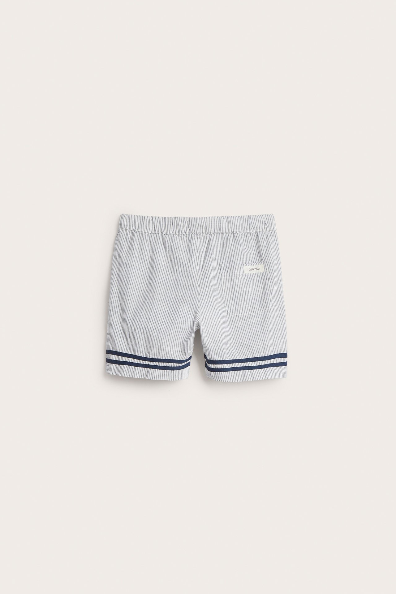 Frontvisning av offwhite stripete barneshorts med elastisk midje og marineblå dobbeltstripete kanter.
